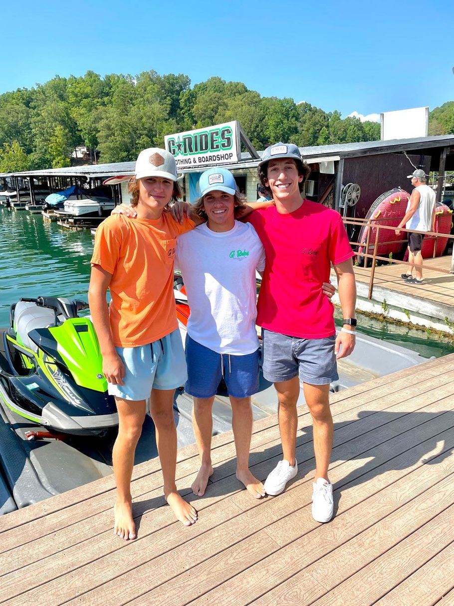 Three young men are posing for a picture on a dock with jet skis in the background