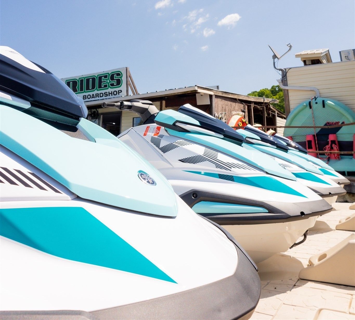 A row of jet skis are parked in front of a store called rides