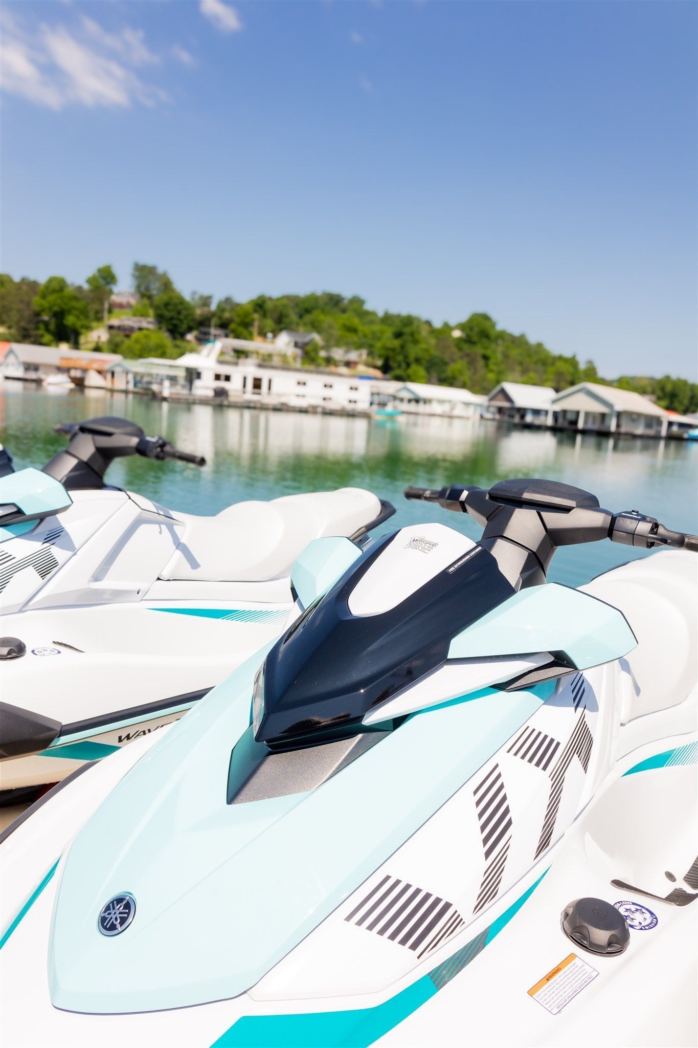 A row of jet skis are parked on the shore of a lake