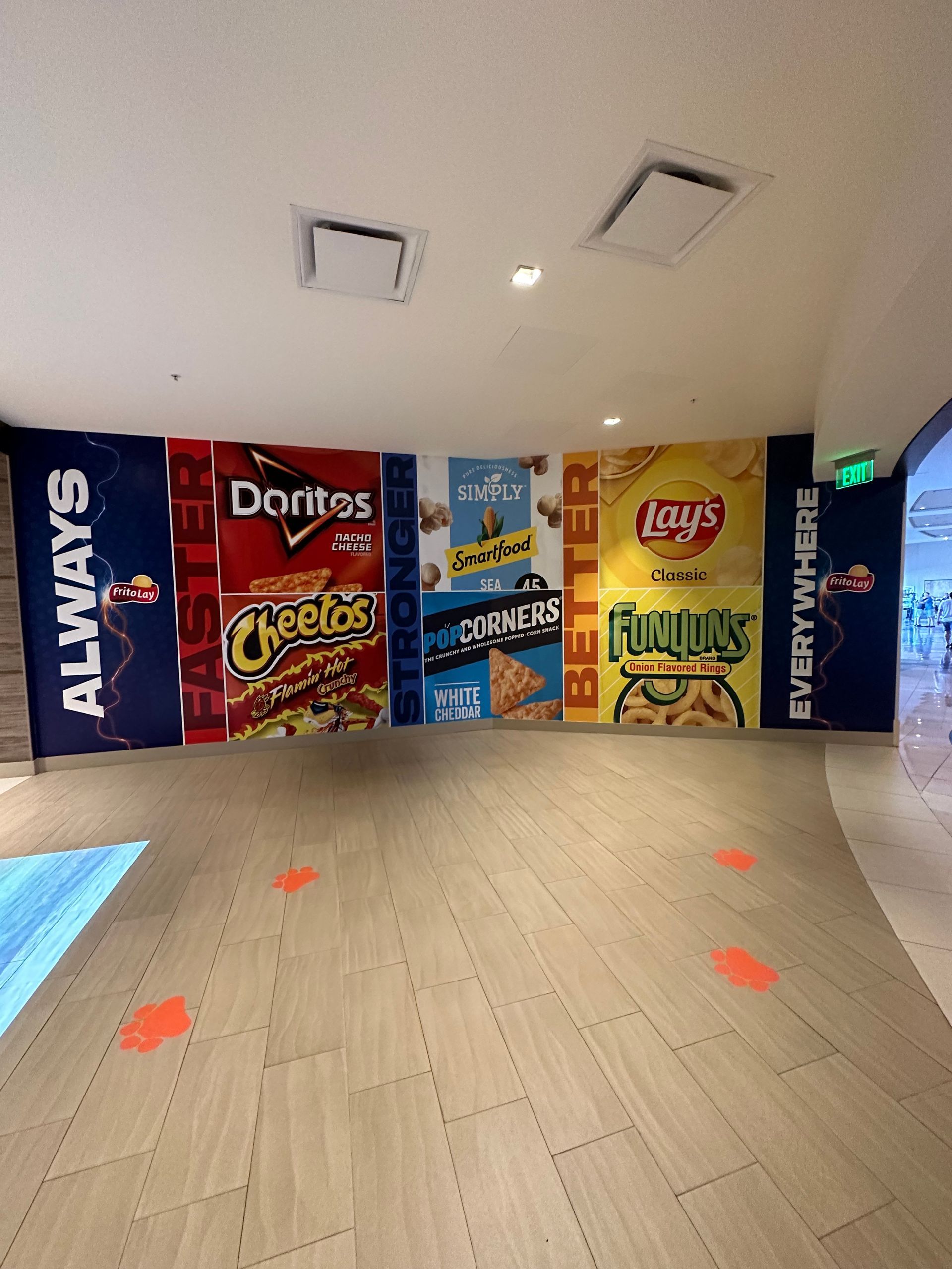 A wall display featuring large posters of popular snack brands like Doritos and Lay's, in a brightly lit indoor space.