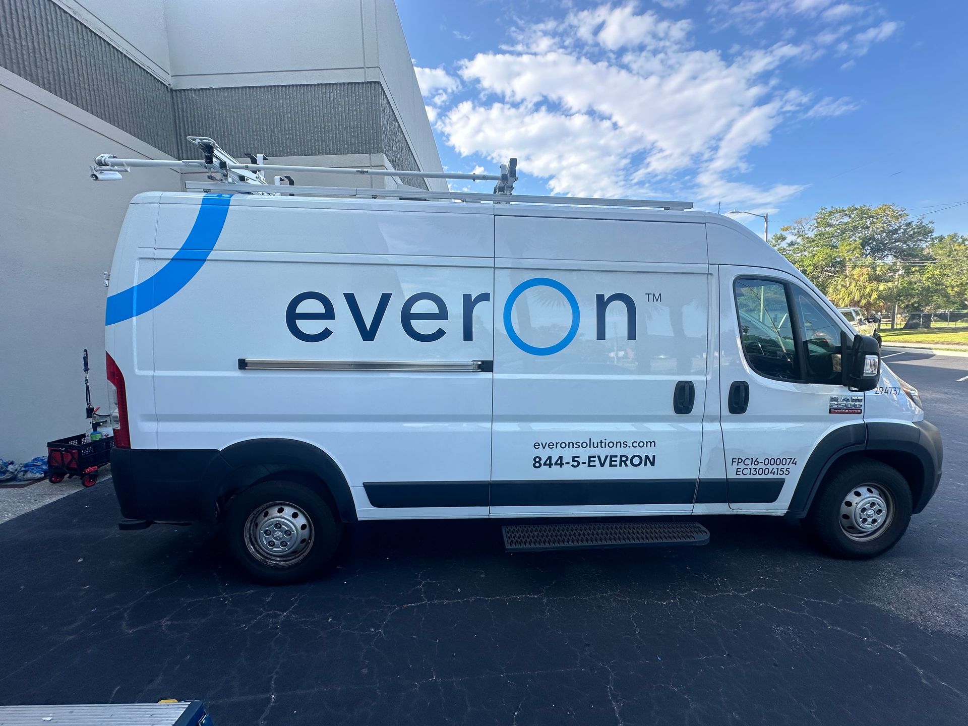 White Everon van with blue accents and logo parked outside. A ladder rack is on the roof.