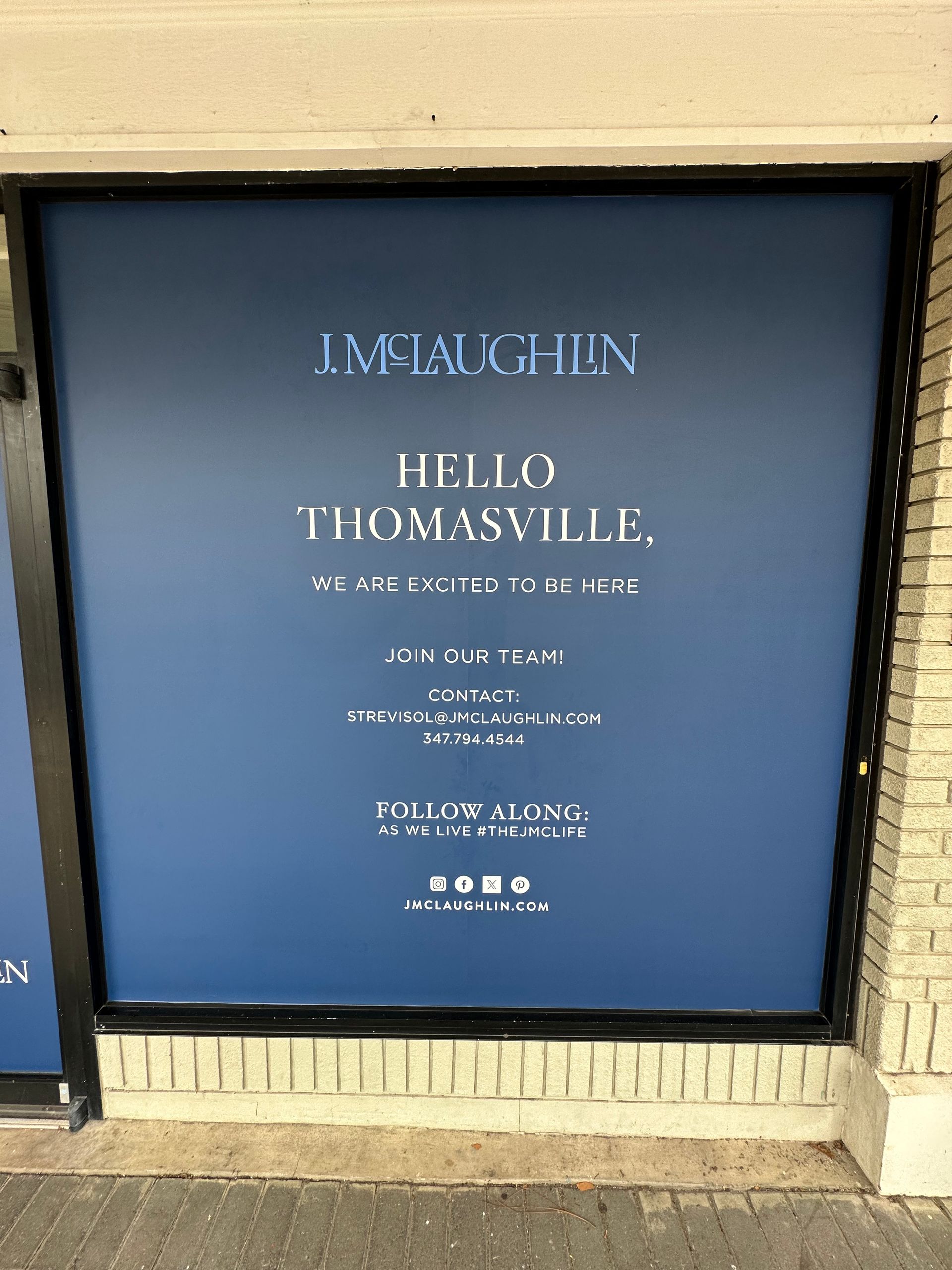 Sign in a storefront window reading "Hello Thomasville," advertising a business called “Lmstaughton,” with contact information. The background is blue.
