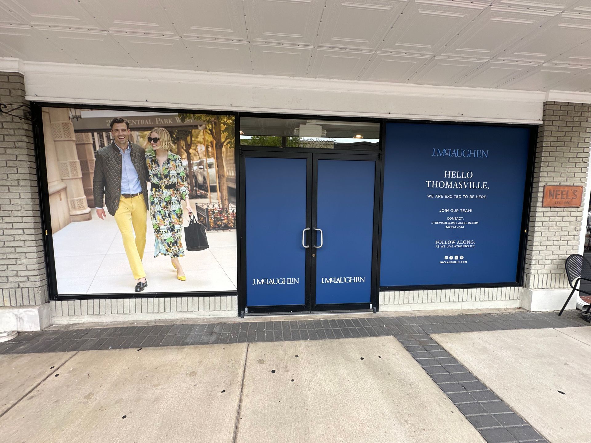 Storefront with a banner of a couple in stylish clothing. The store has blue panels and signage for 