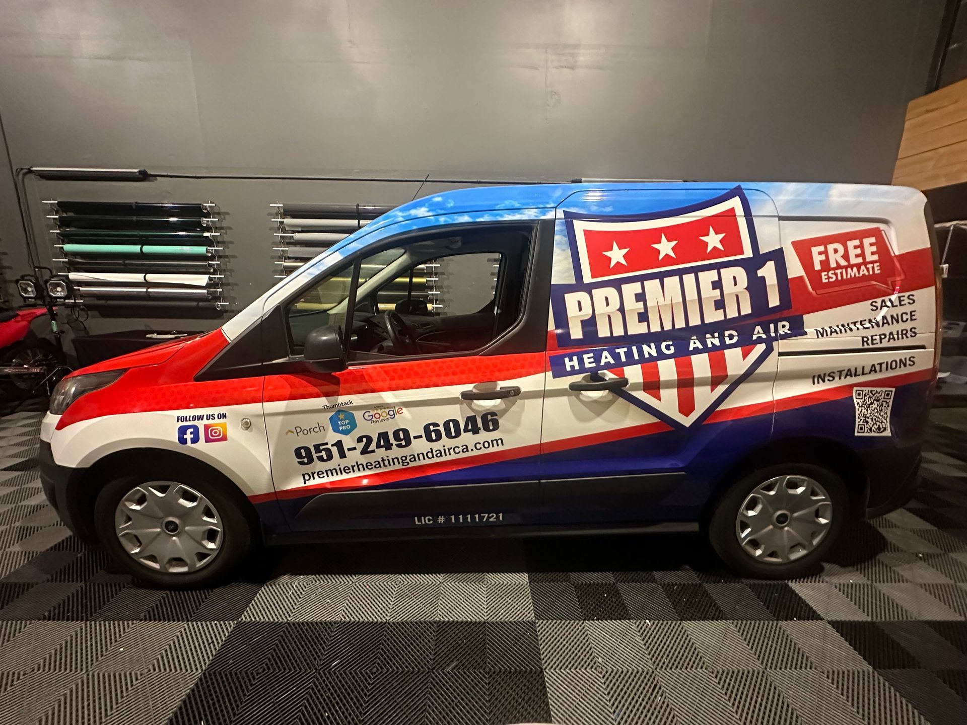 A van with a patriotic wrap featuring the company logo "Premier 1 Heating and Air". The van is parked indoors.