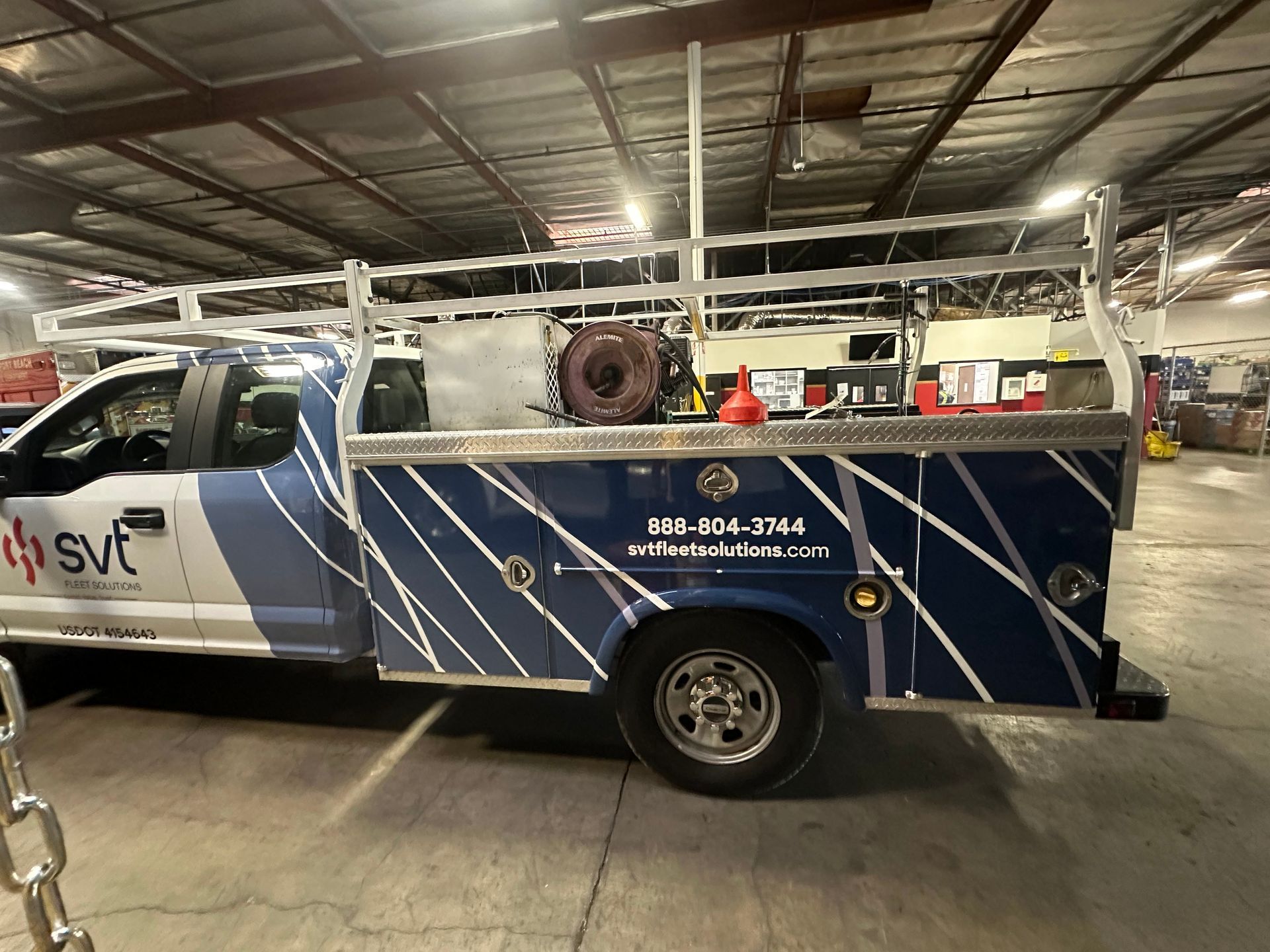 A utility truck with a custom toolbox and ladder rack, sporting a blue and white company logo, parked inside a warehouse.