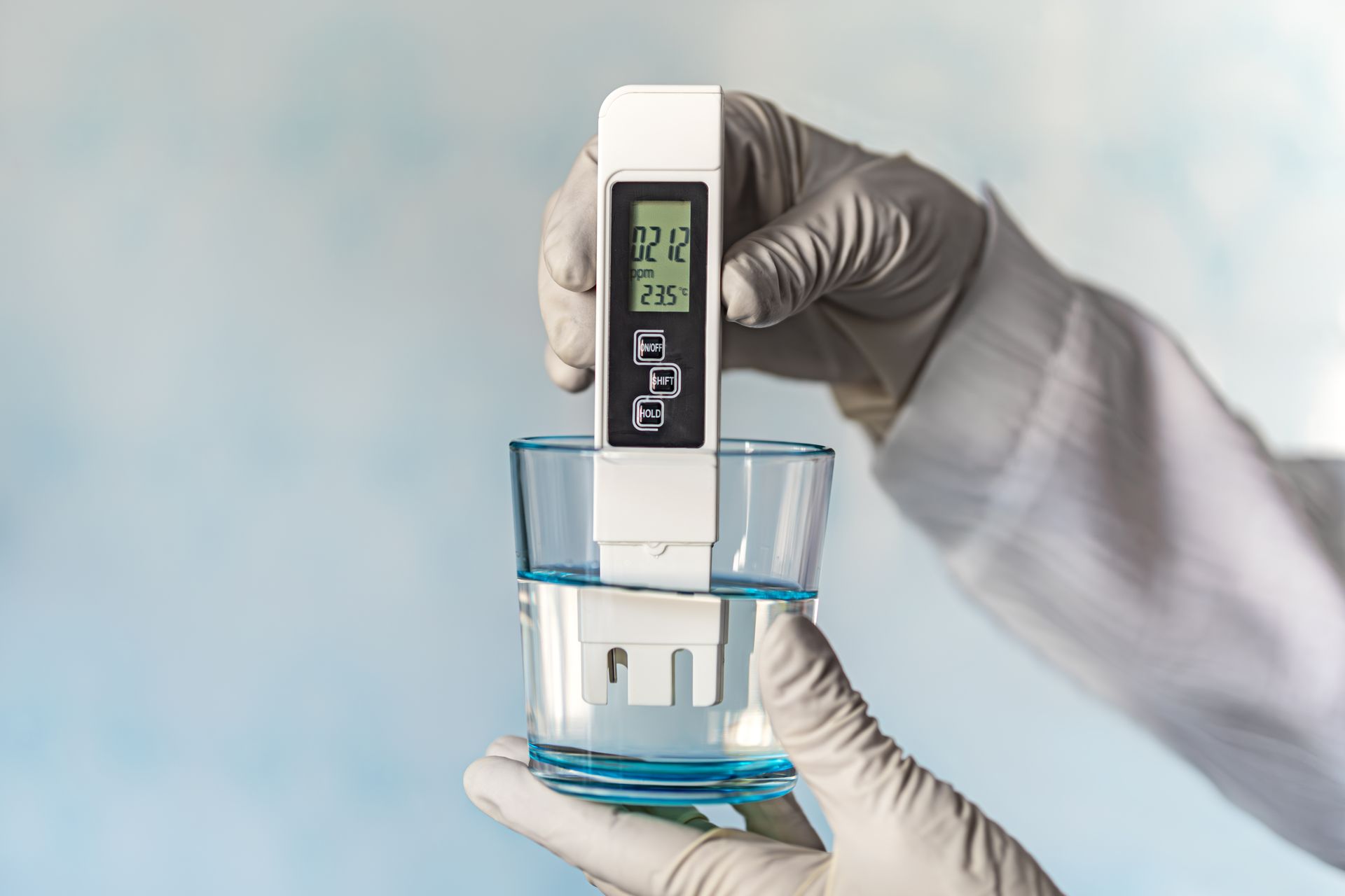 A person is holding a digital thermometer over a glass of water.