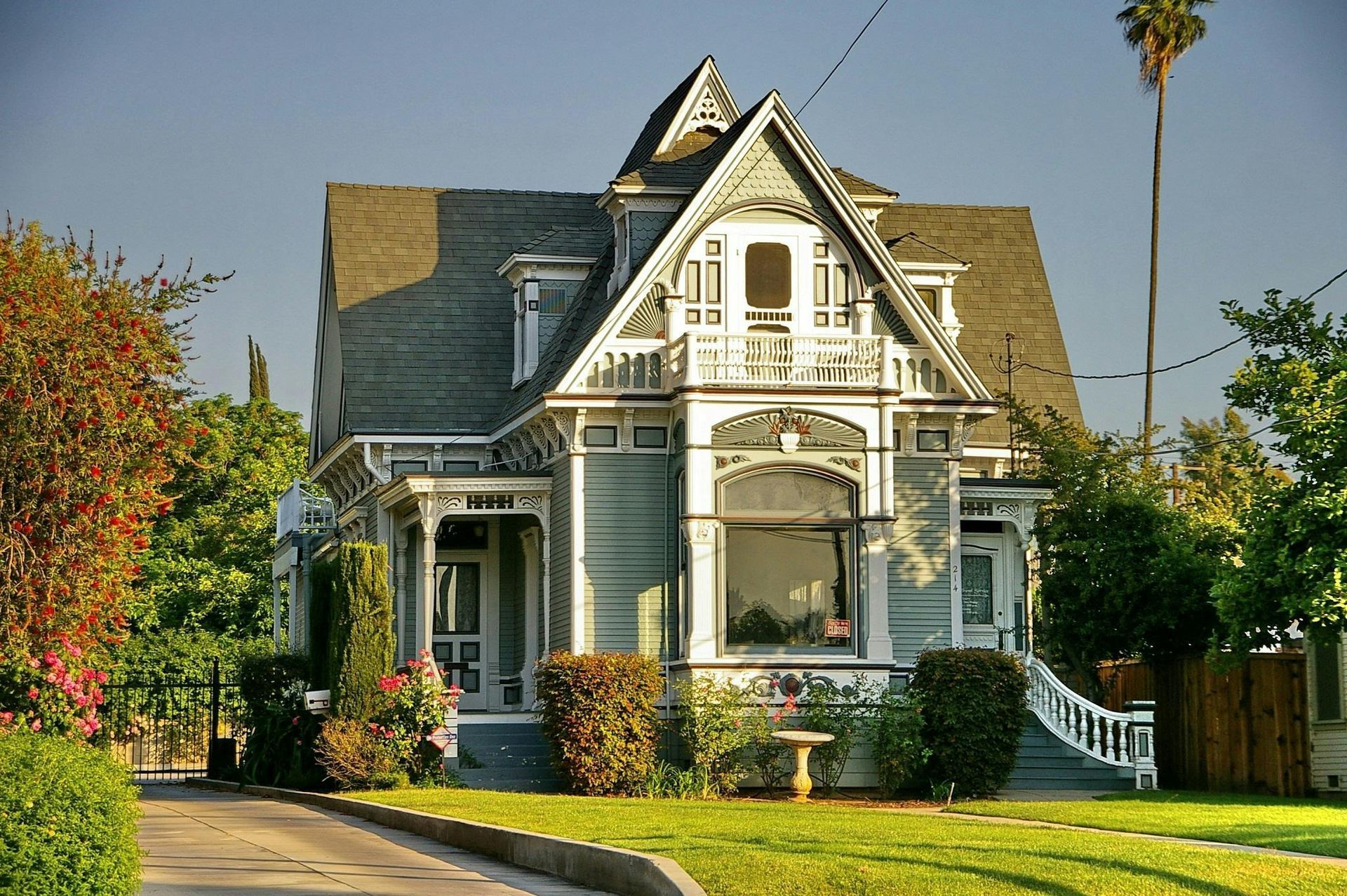 Victorian-style light blue house with detailed trim and a dark gray roof, surrounded by trees and a lawn.
