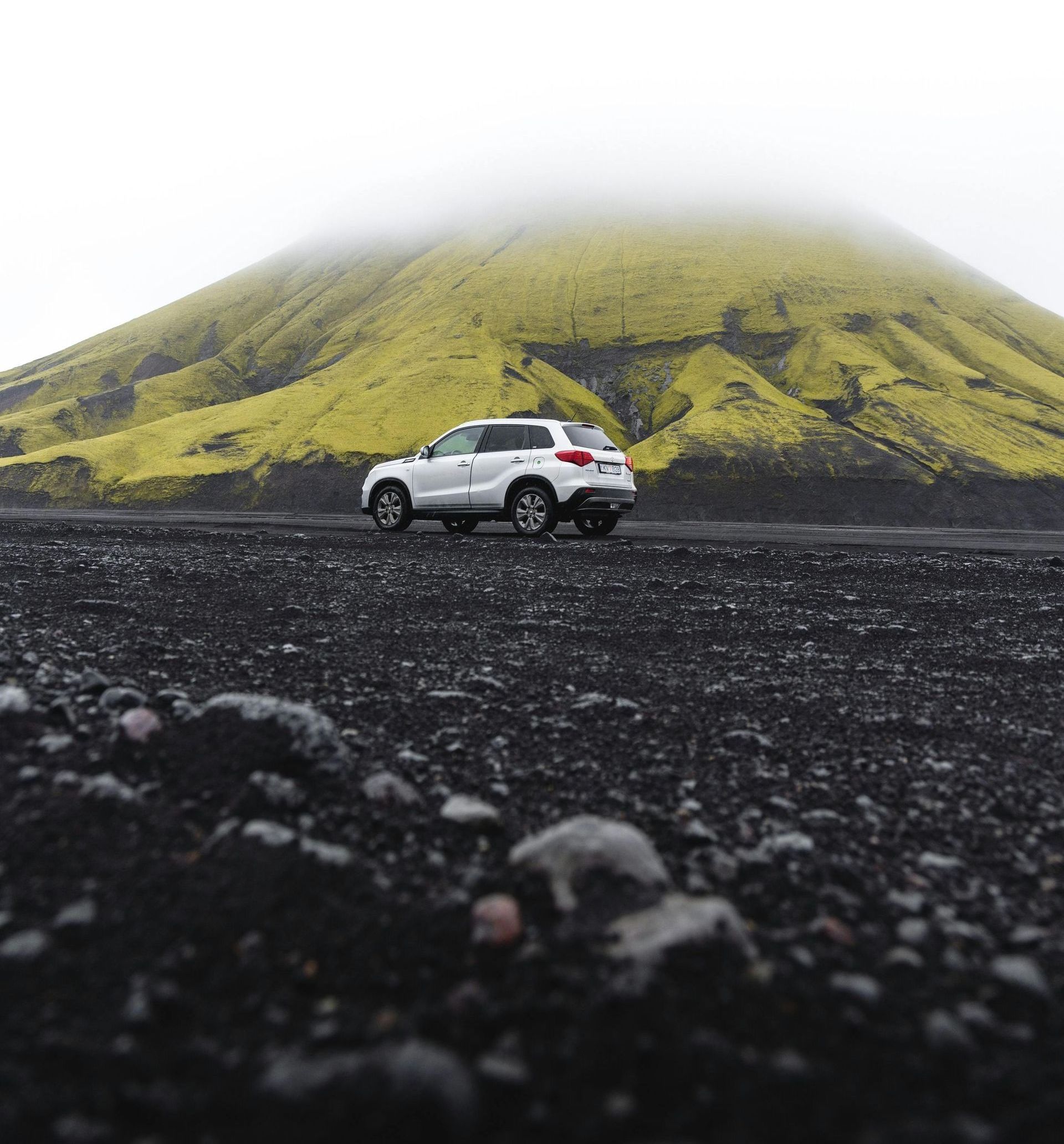 A car is driving down a dirt road in front of a mountain.