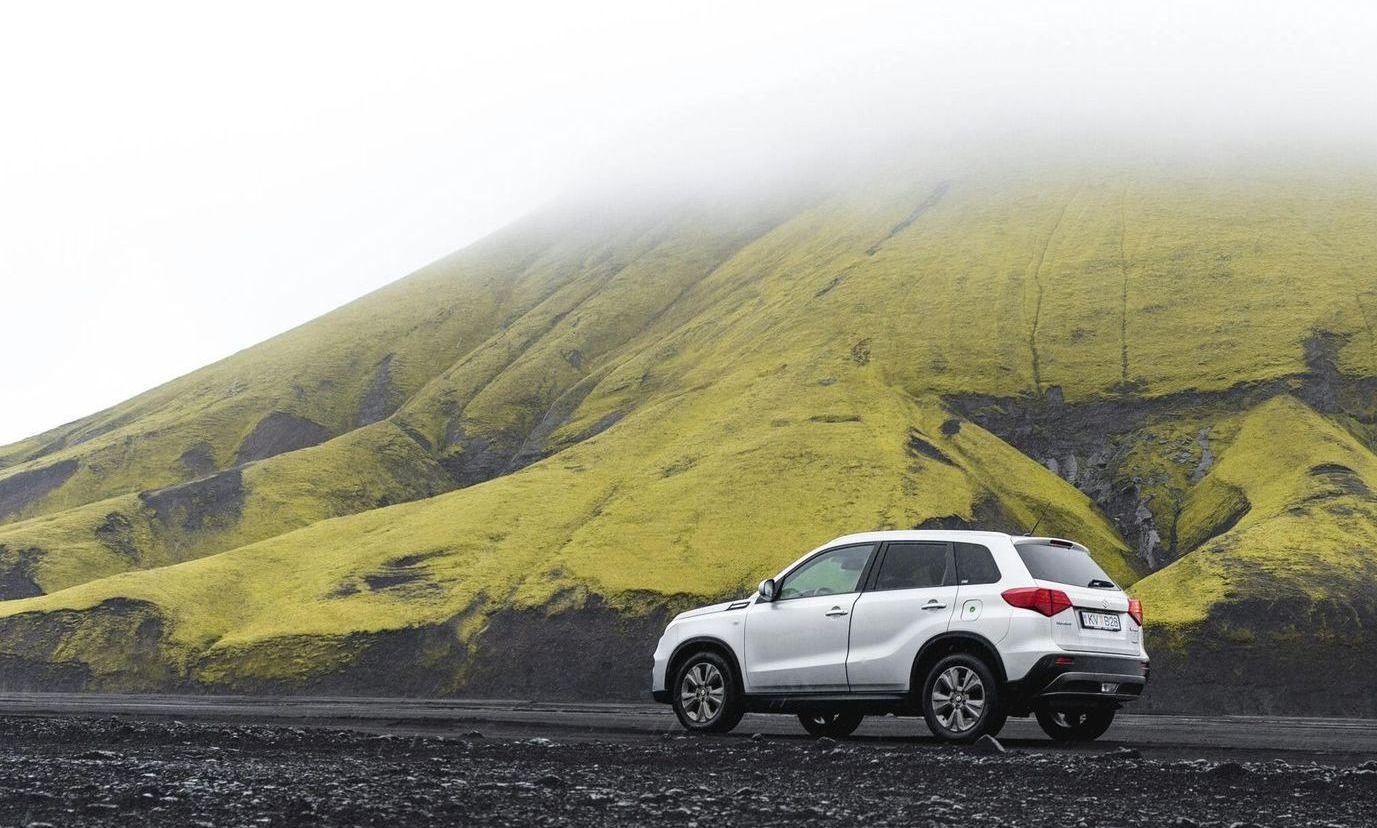 A white suv is parked on the side of a road in front of a mountain.
