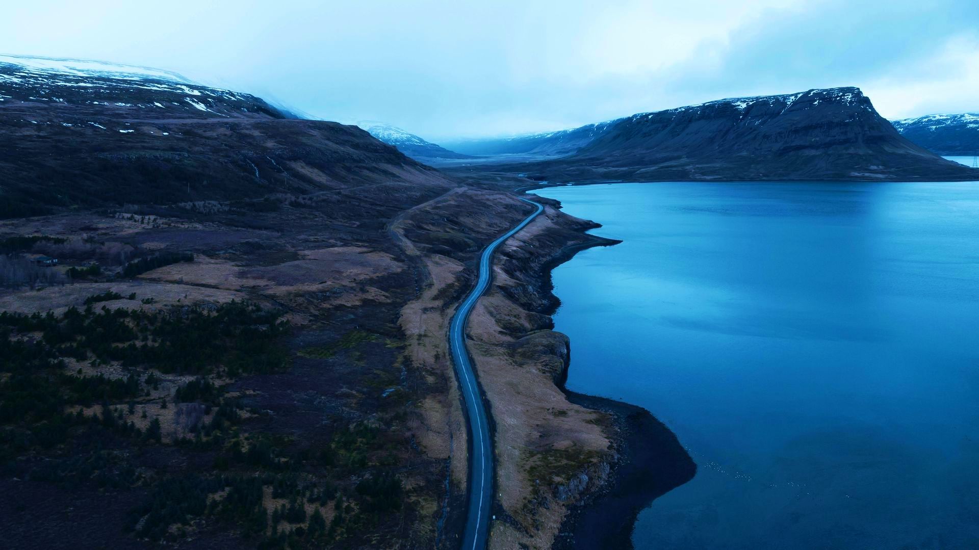 An aerial view of a road going through a lake surrounded by mountains.