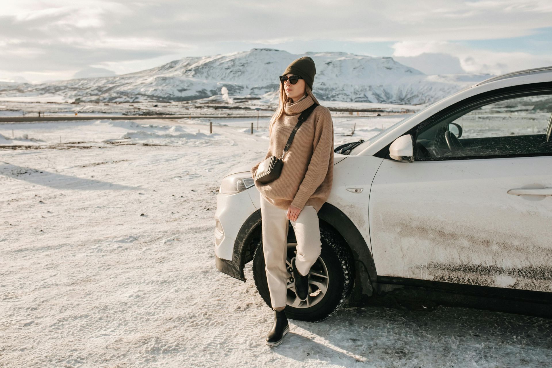 A woman is leaning against a white car in the snow.