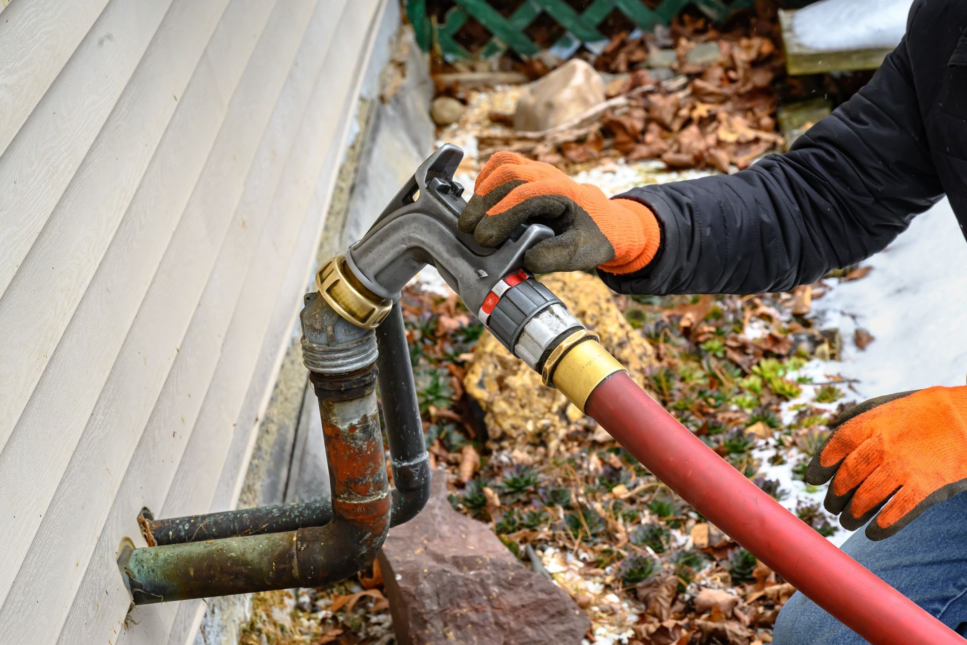 A gloved technician connecting a heating oil delivery nozzle to an outdoor fill pipe at a home