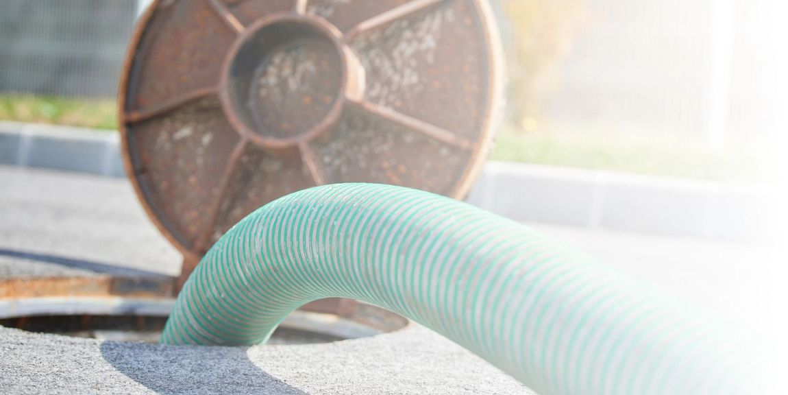 A green hose is coming out of a manhole cover.