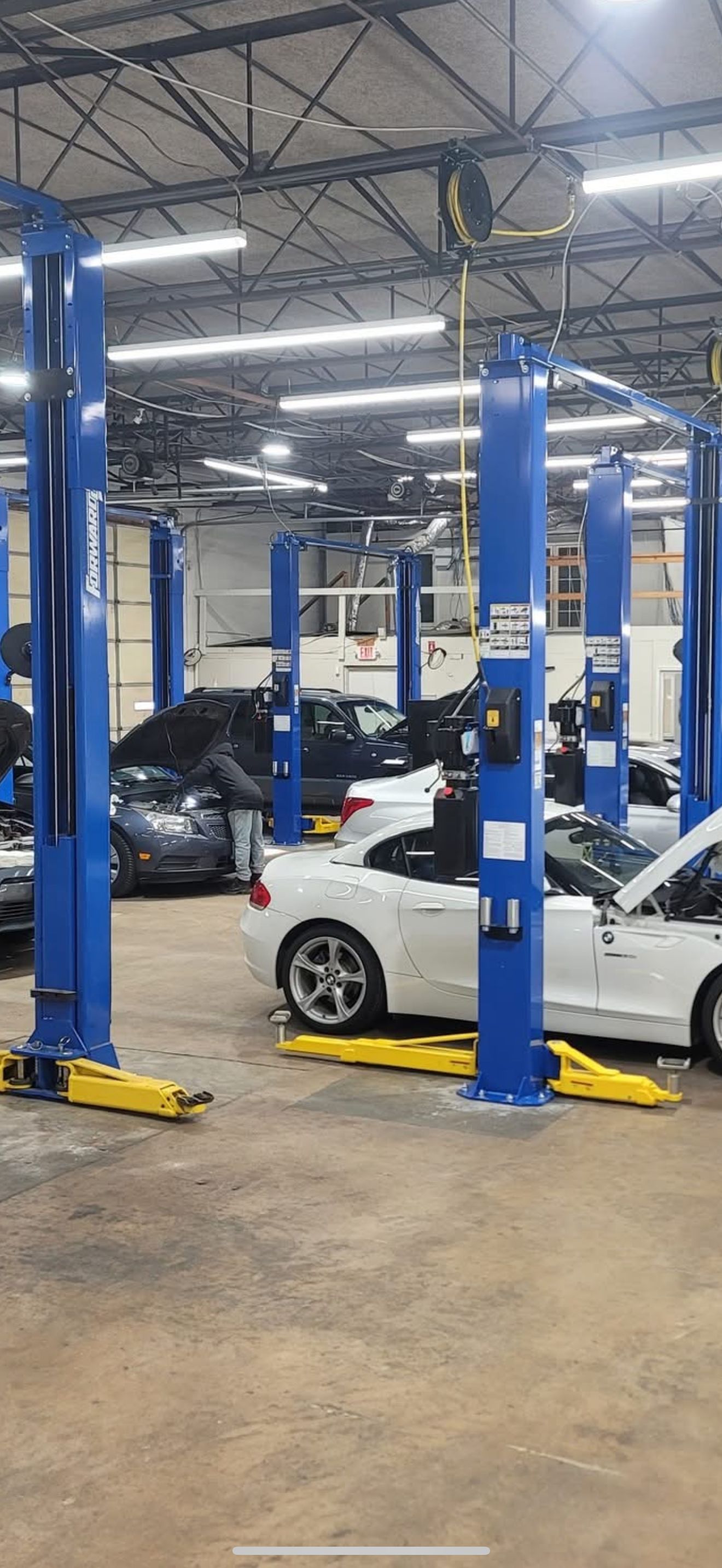 Blue car lifts in a car repair shop. White and black cars on the lifts. | Zach's Auto Clinic
