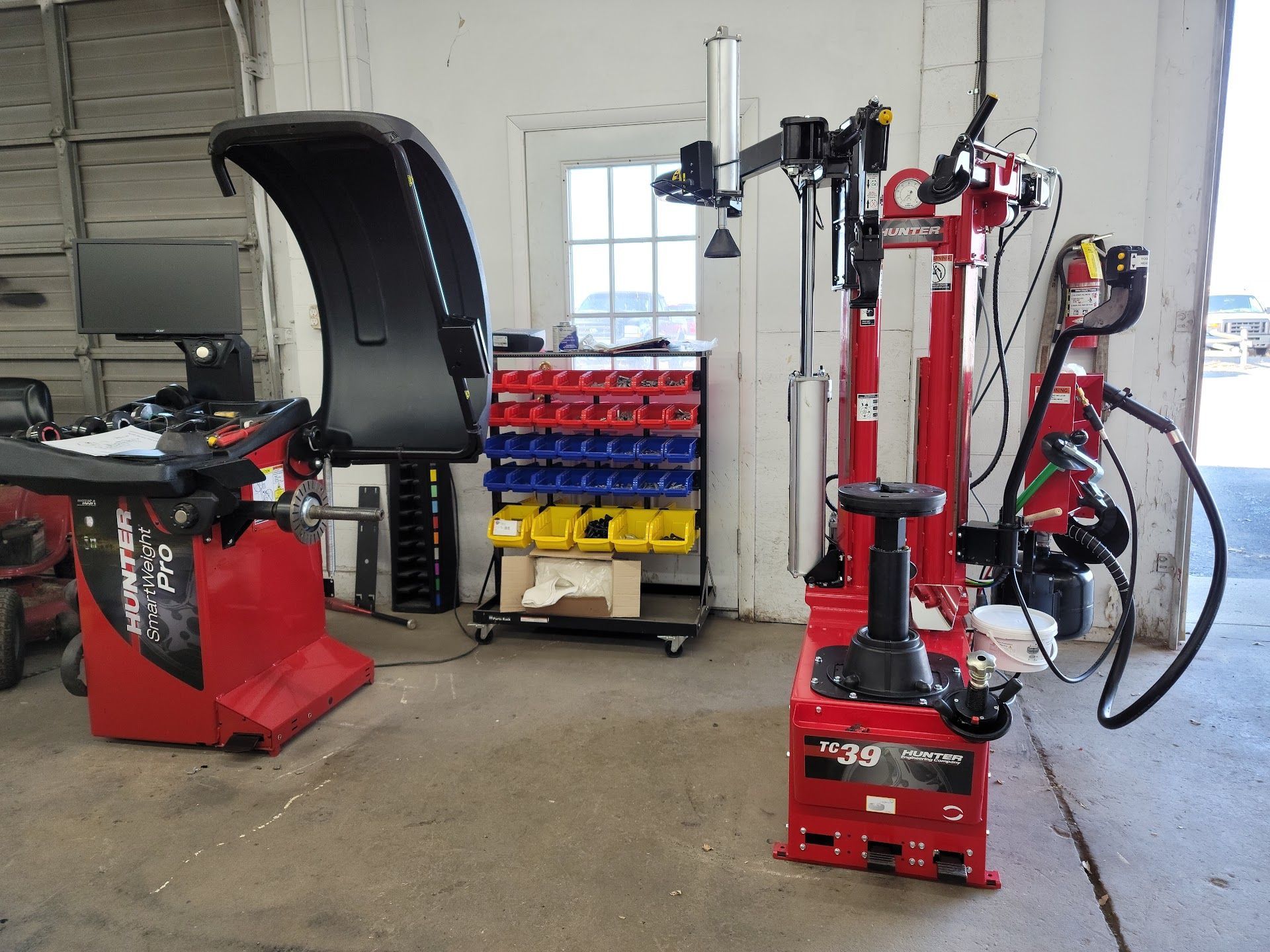 Garage scene with tire changing and balancing equipment. Red machines, bins of parts, open doorway. | Zach's Auto Clinic