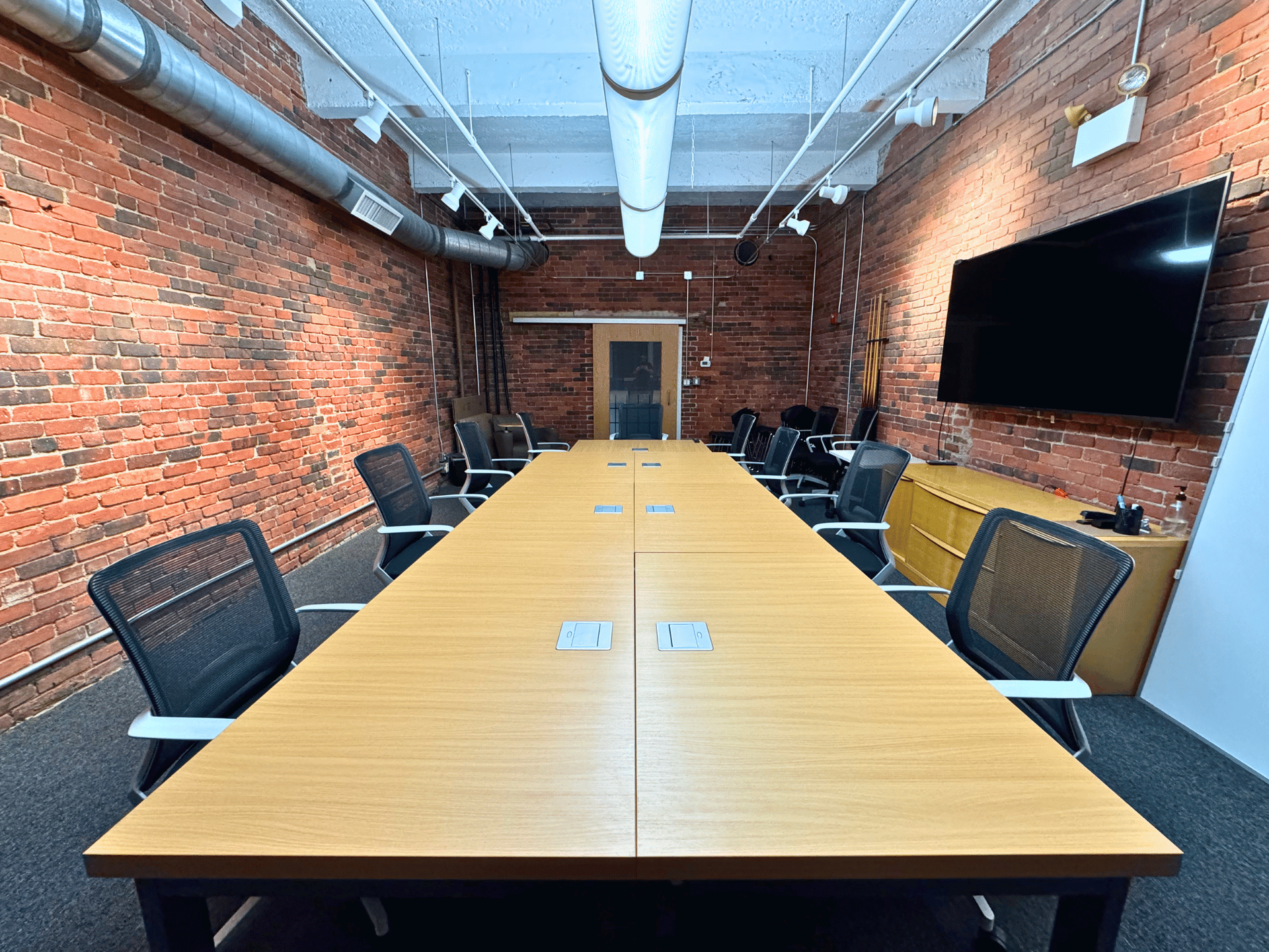 A conference room in a commercial office with a long table and chairs and a flat screen tv in Boston MA. This office is cleaned by ThinkFast Cleaning Services.