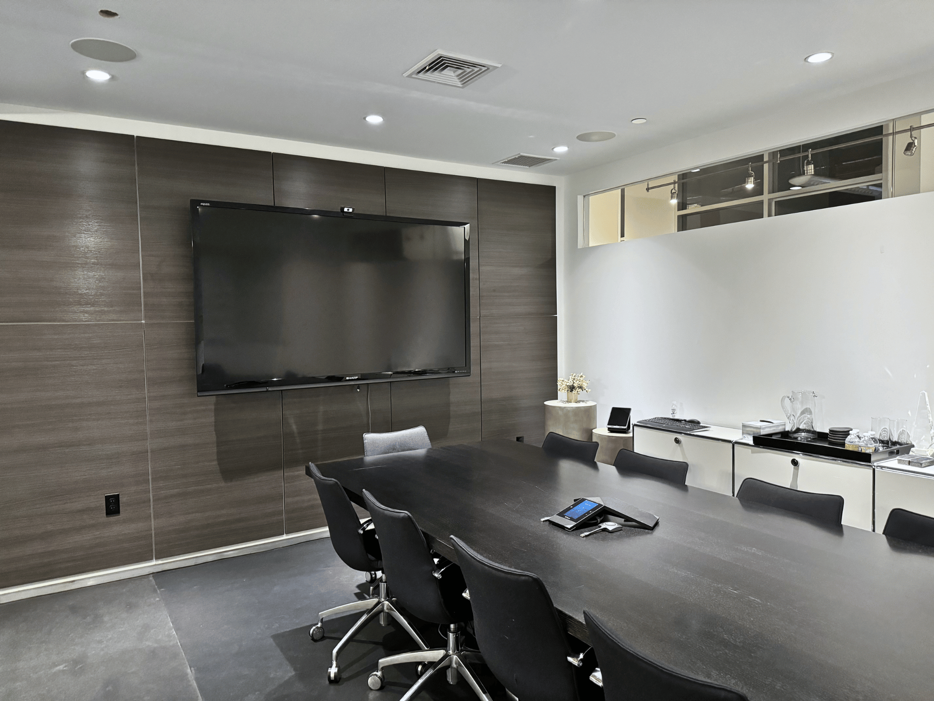 A conference room with a long table and chairs and a large flat screen tv on the wall in a commercial office in Boston MA. This office conference room is cleaned by ThinkFast Cleaning Services.