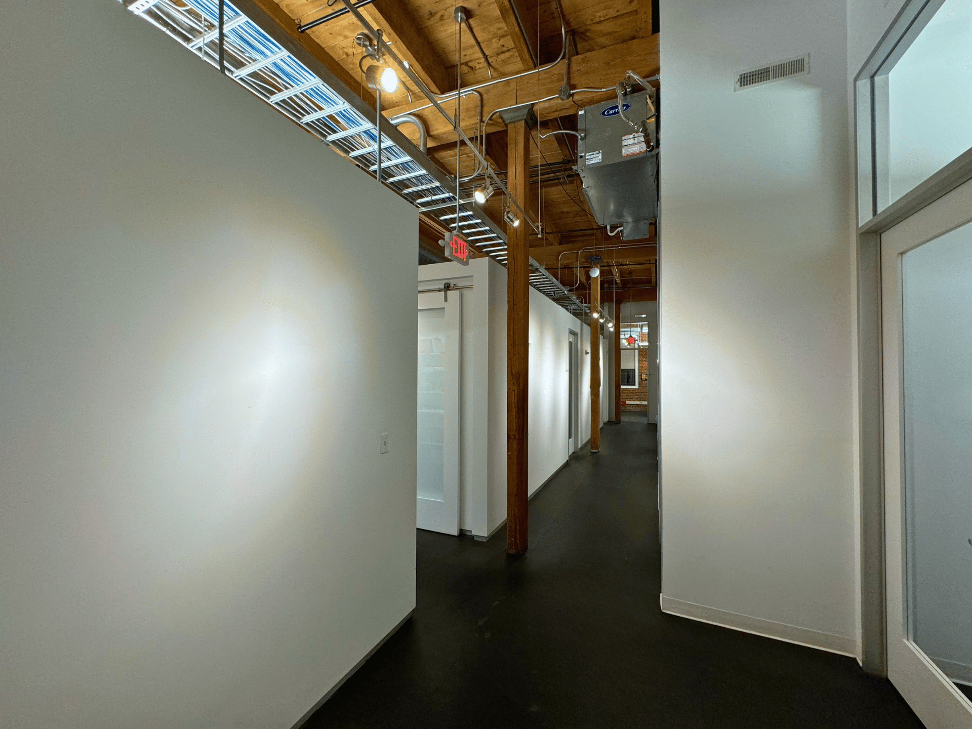A long hallway with white walls and black floors; a commercial office in Boston MA. This office's hallway and cubicles are cleaned by ThinkFast Cleaning Services.