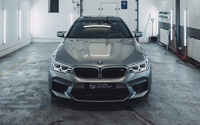 Gray BMW M5 sedan parked in a garage with overhead lighting.