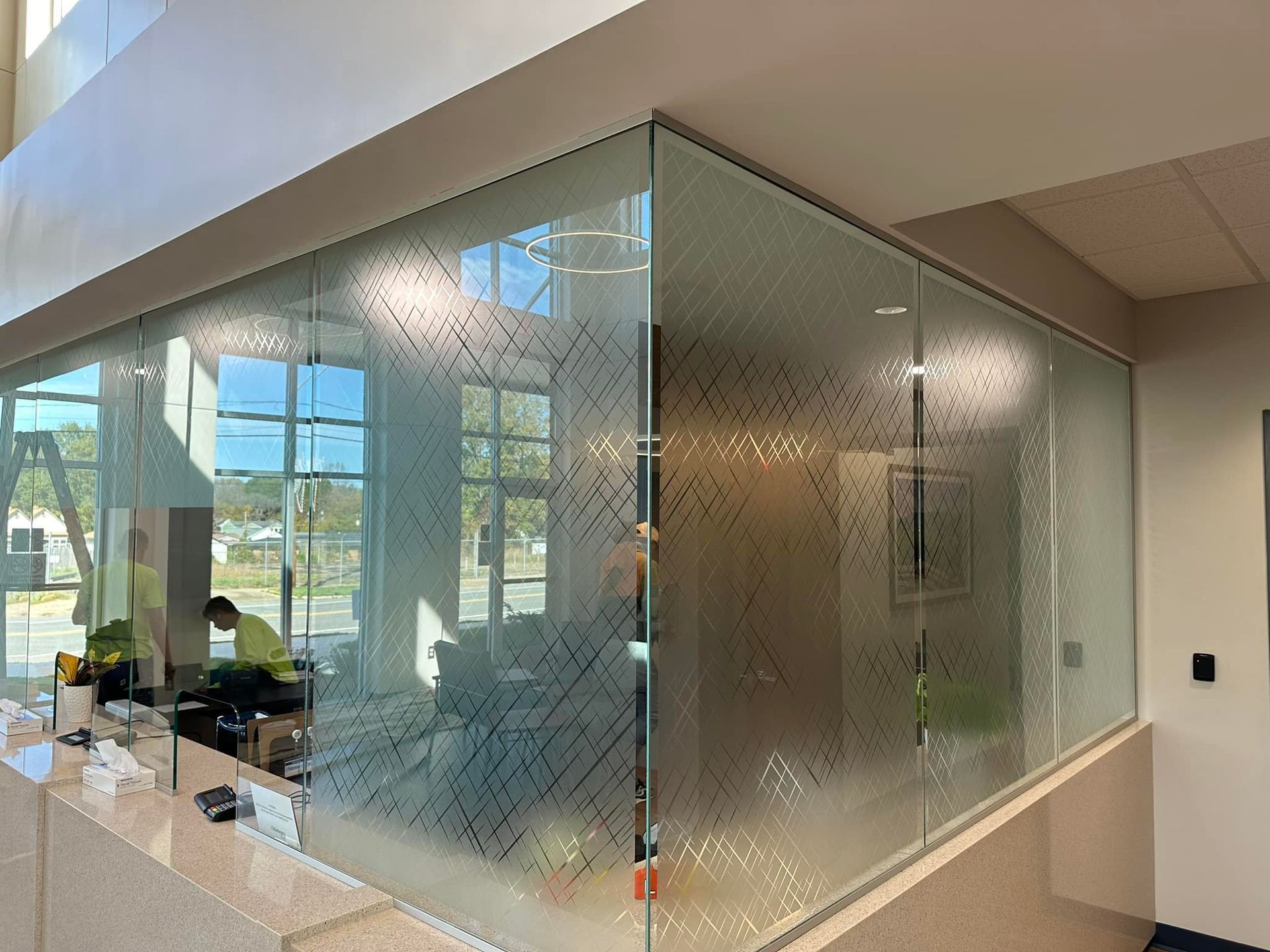Glass office partition with patterned frosting, separating a reception area. Sunlight streams in.
