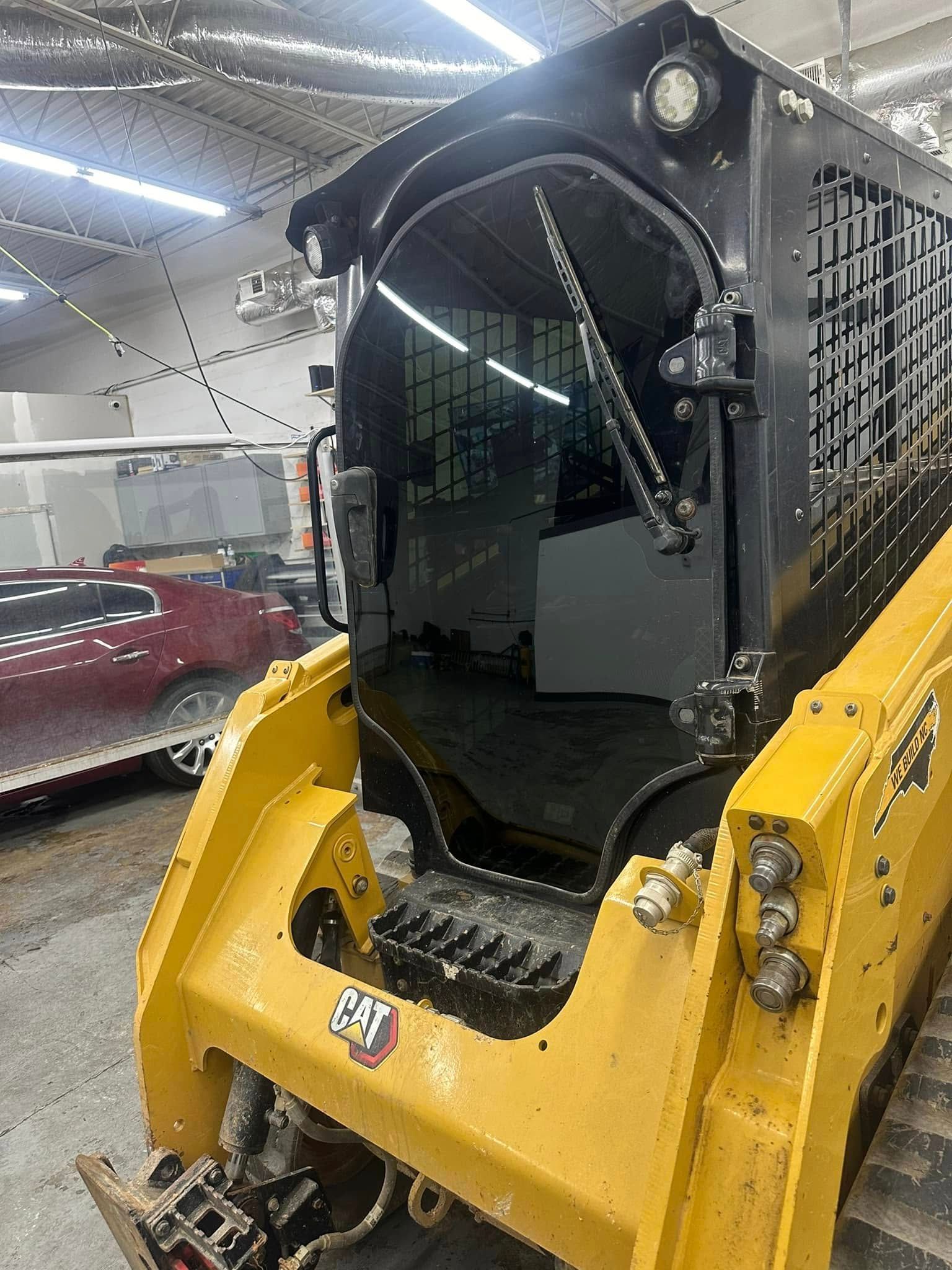 Yellow and black skid steer with enclosed cab. Inside a building.