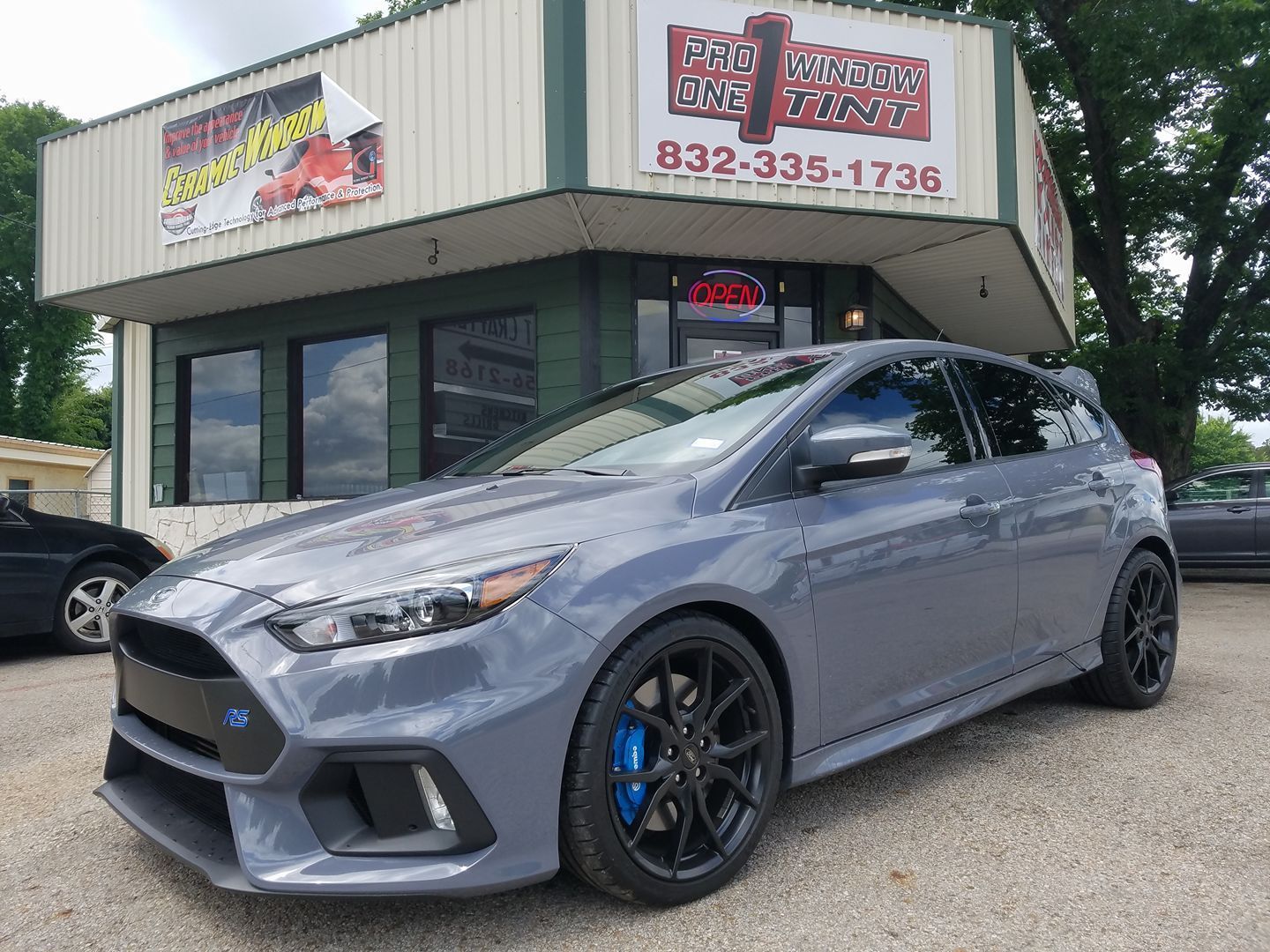 Gray Ford Focus RS in front of a shop with a sign and phone number, 832-335-1736.