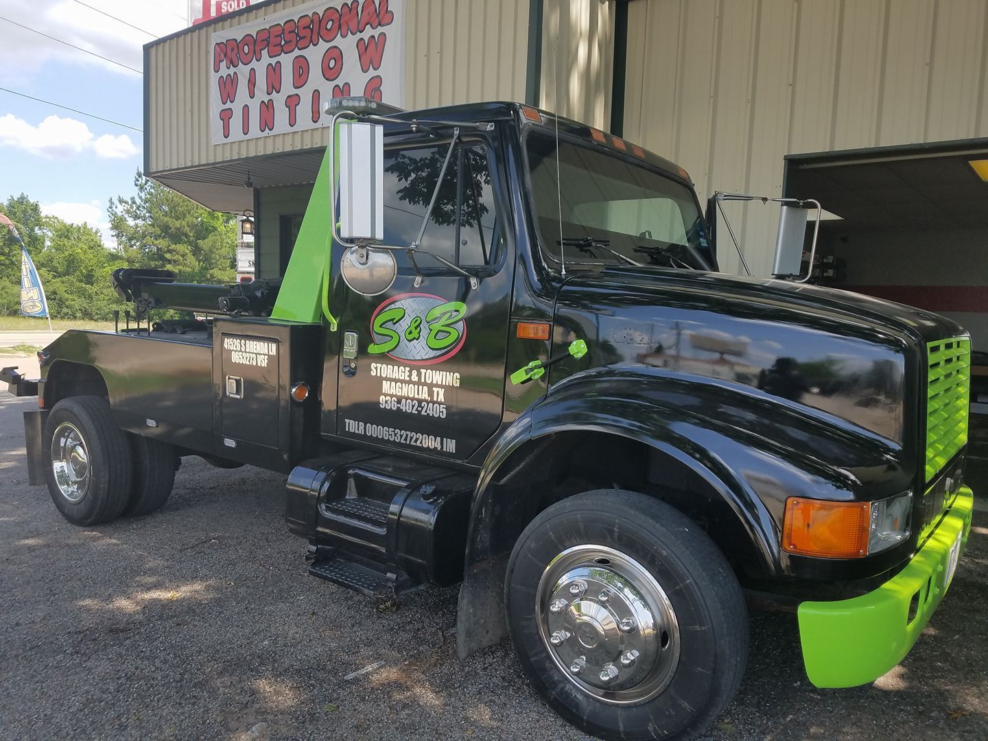 Black tow truck with lime green accents, parked outside a Professional Window Tinting business.