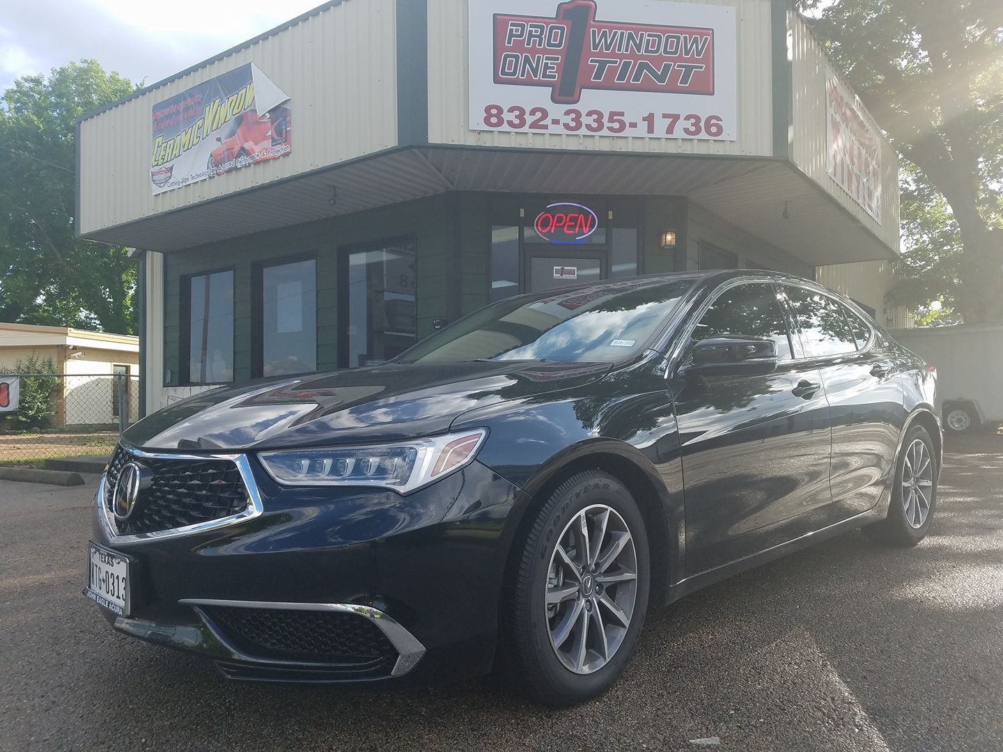 Black Acura sedan parked in front of a building with a business sign, phone number 832-335-1736.