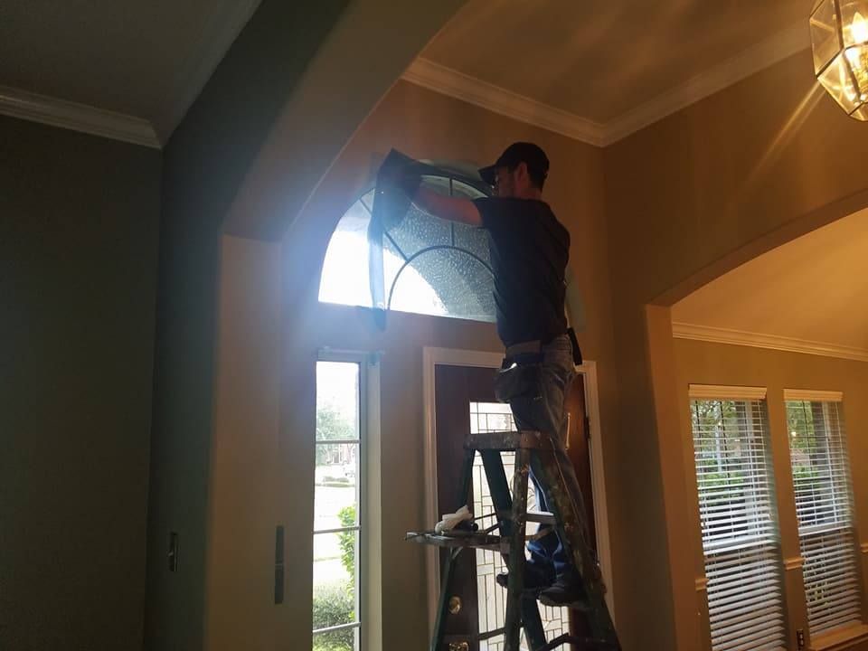 Person on ladder applying film to an arched window. Indoors, natural light, working on entry door.
