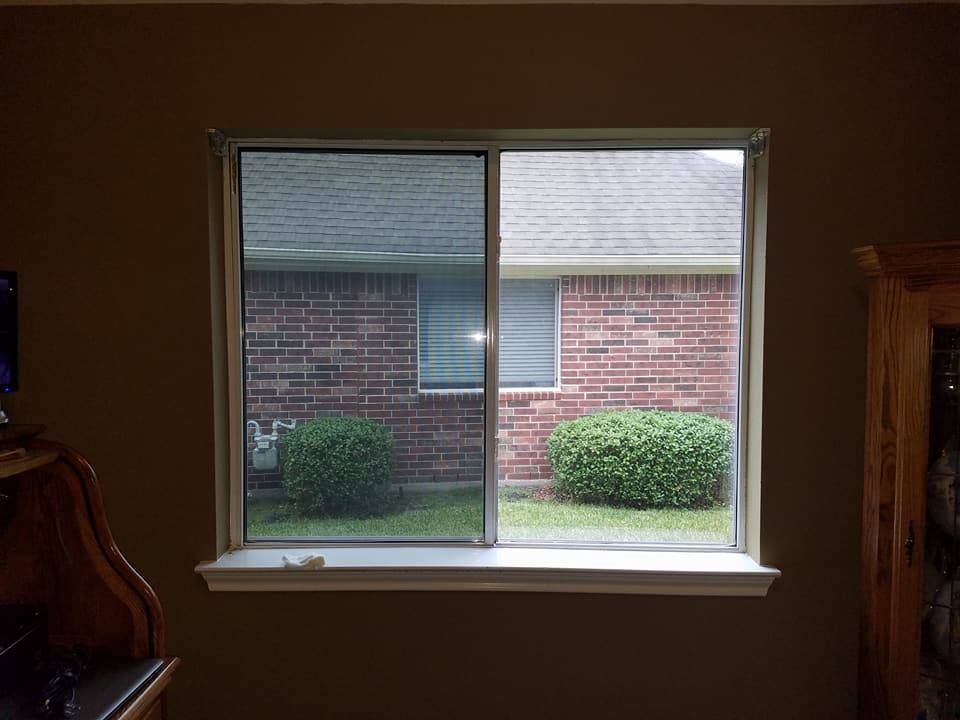 A window with a partial screen, looking out onto a brick building and green bushes.