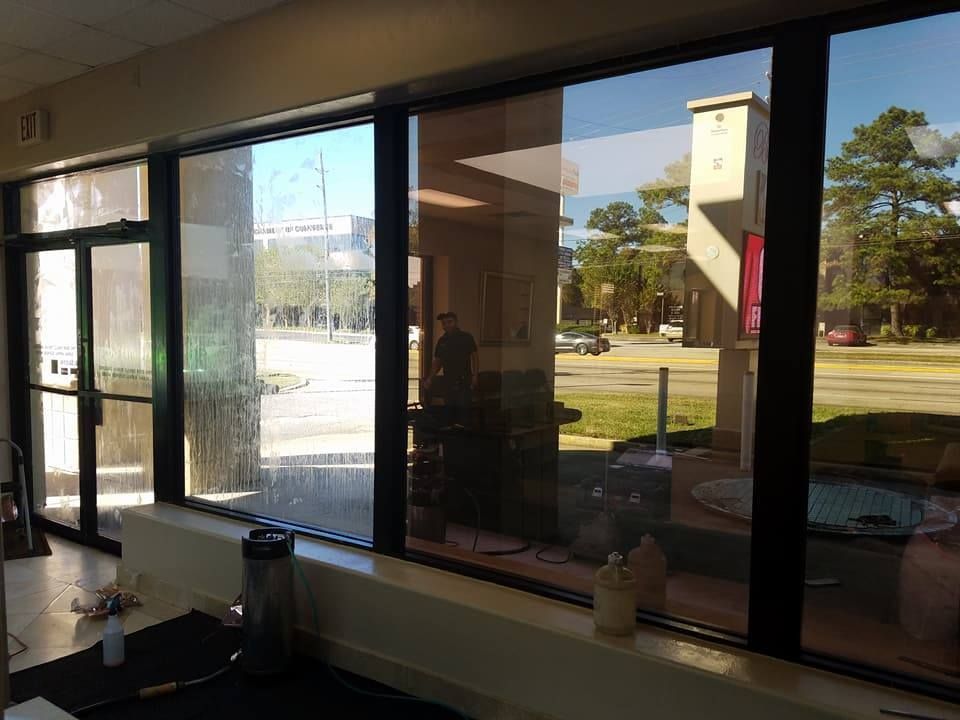 Interior view of windows overlooking a sunny street with a building and trees.