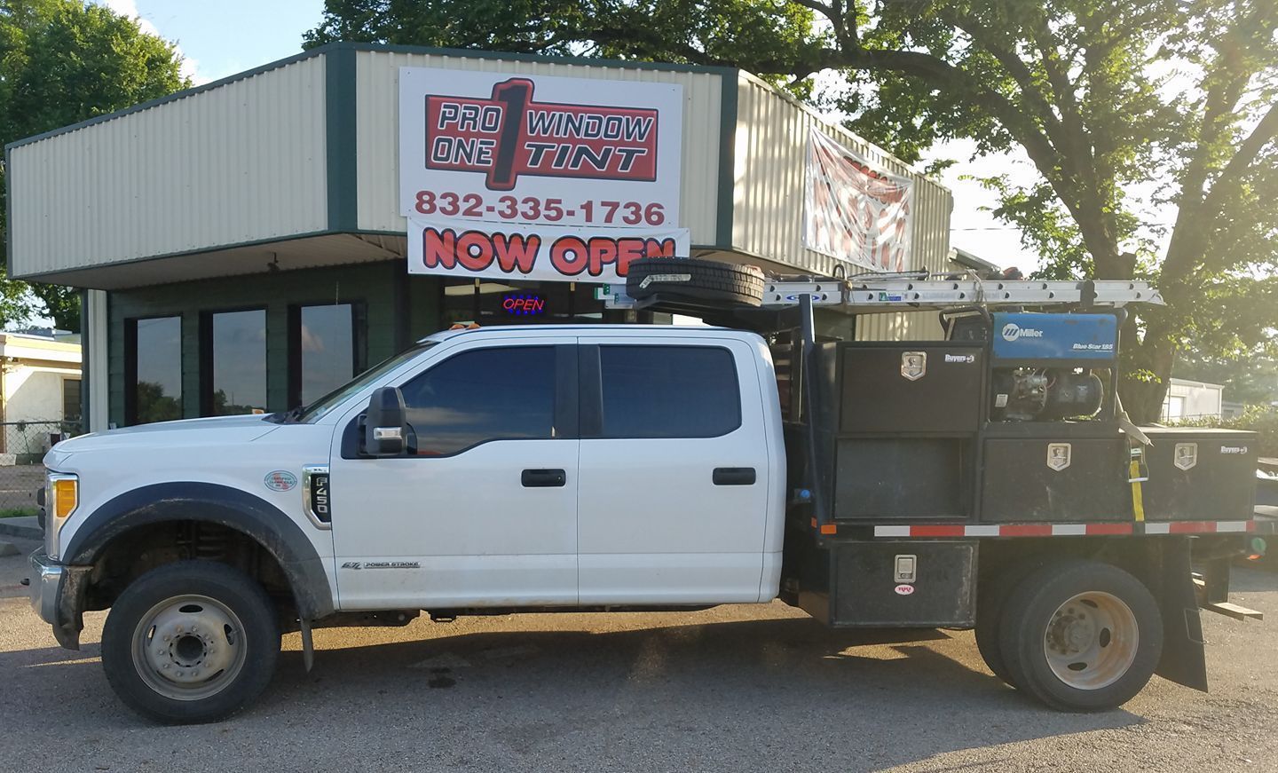 White Ford truck with equipment on its bed parked in front of a building with a sign that says 