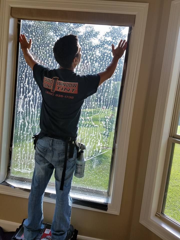 Person applying film to a window. Standing with arms outstretched, applying wet film. Window has green outdoor view.