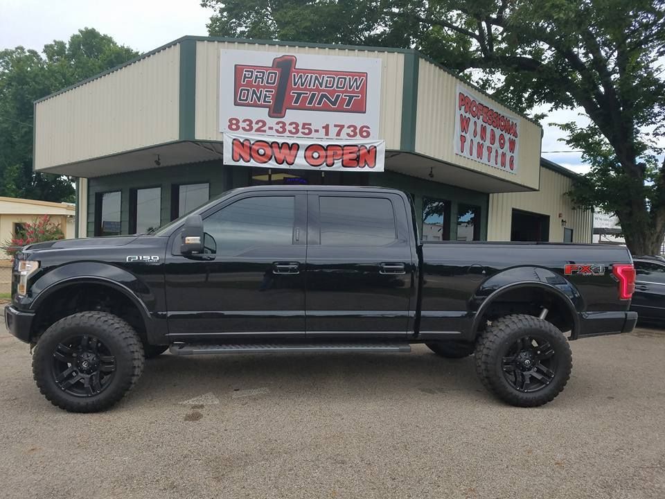Black Ford F-150 truck with tinted windows parked in front of a building with a business sign.
