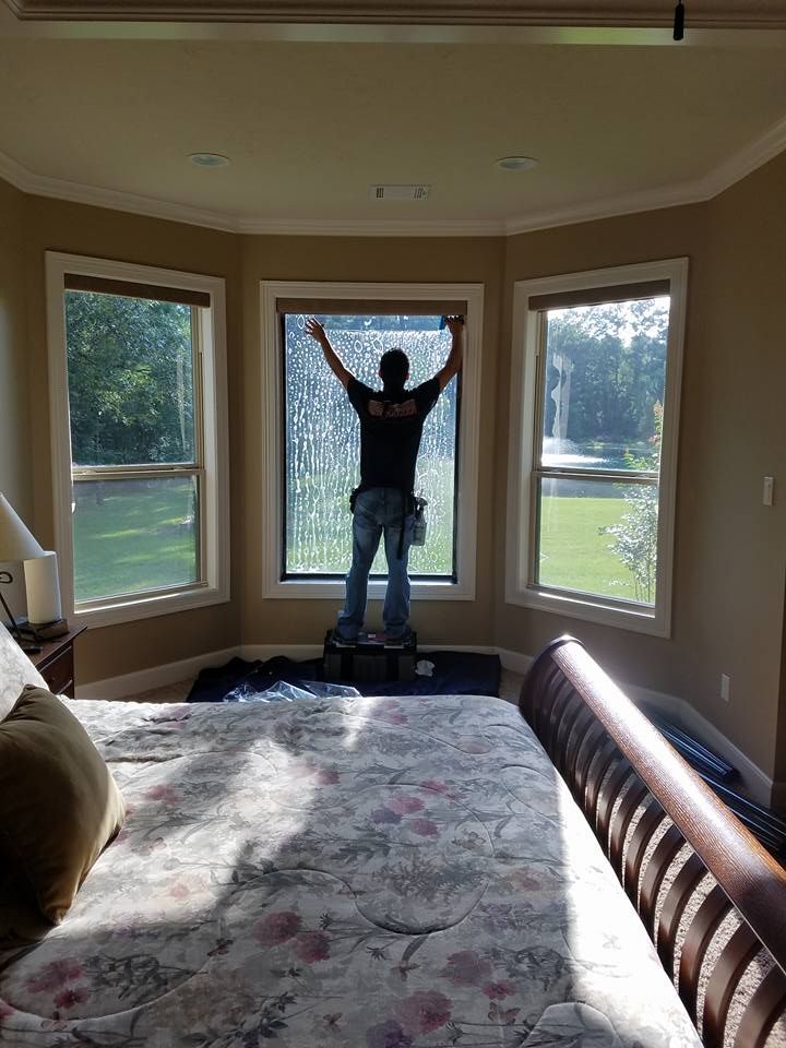 Person applying tint to a window in a bedroom with a bed.