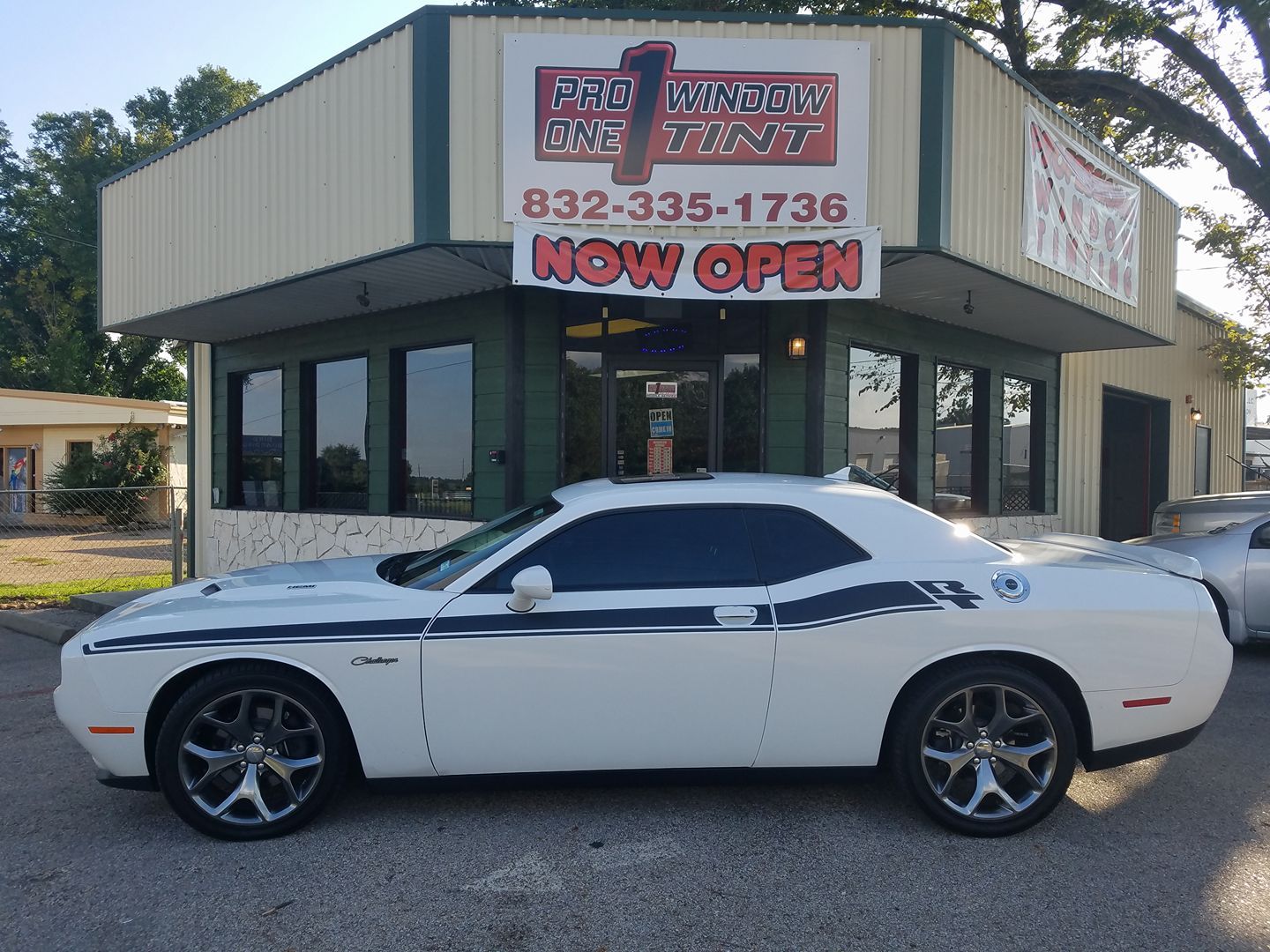 White Dodge Challenger in front of a storefront; business sign says 
