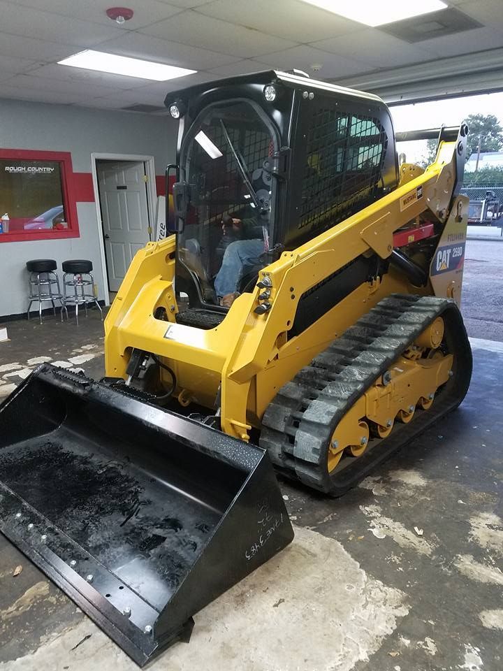 Yellow and black Caterpillar skid steer loader with bucket attachment, inside a garage.