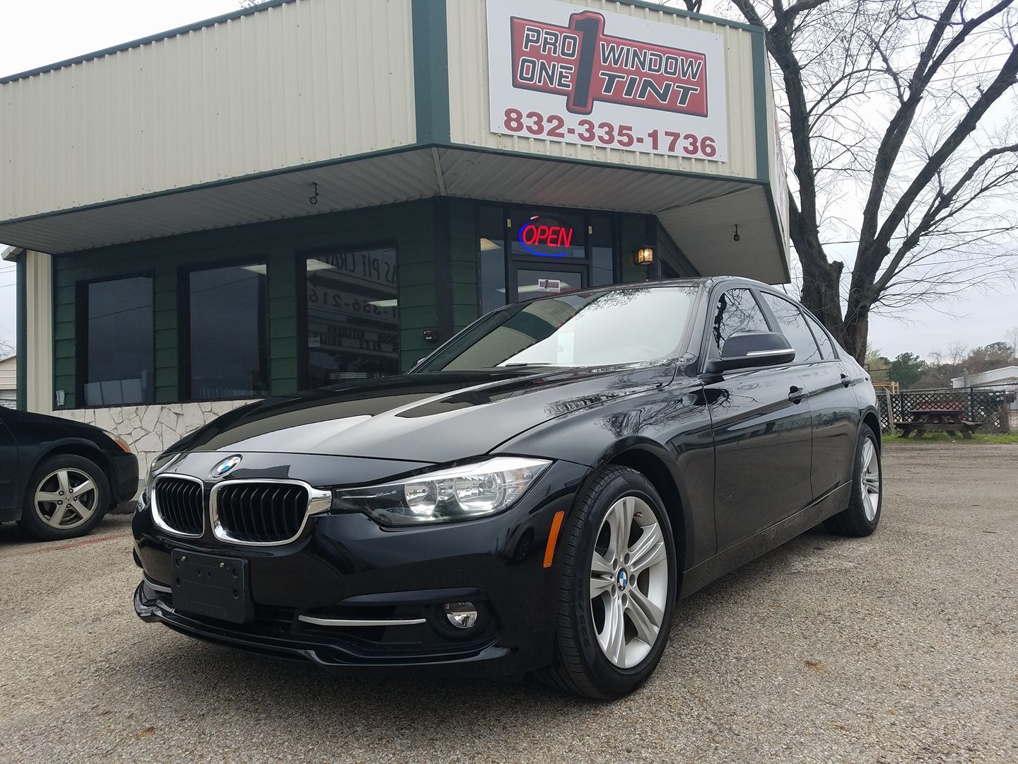Black BMW sedan parked in front of a car dealership, with the phone number 832-335-1736 visible.
