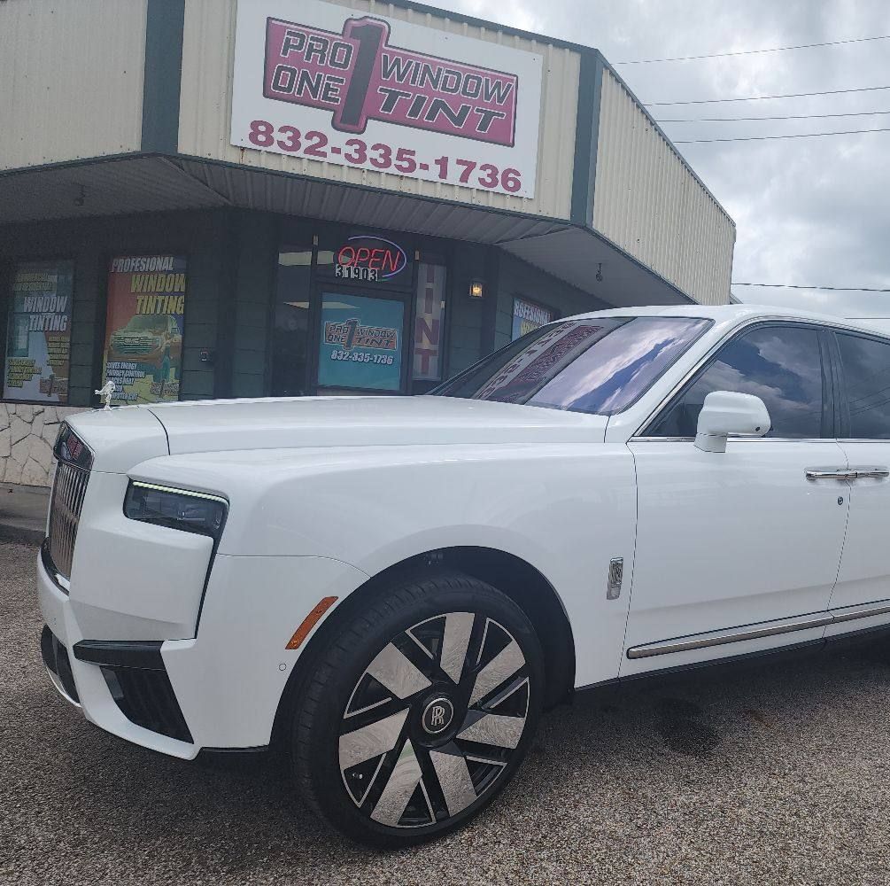 White Rolls-Royce SUV in front of a window tint shop; shop sign displays phone number.