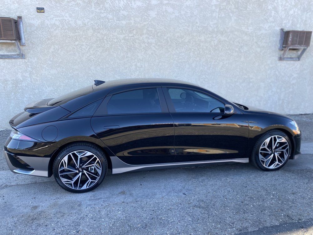 Black Hyundai Ioniq 6 electric car parked outside, angled view, silver trim, and custom wheels.