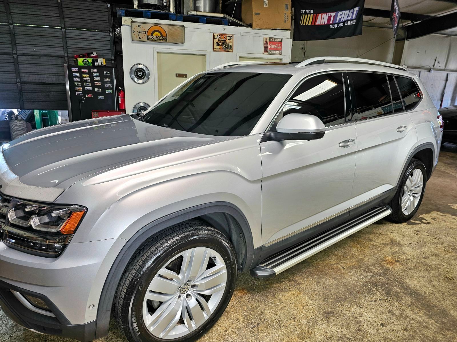 Silver Volkswagen SUV with tinted windows parked inside a shop, side step bars, and shiny wheels.