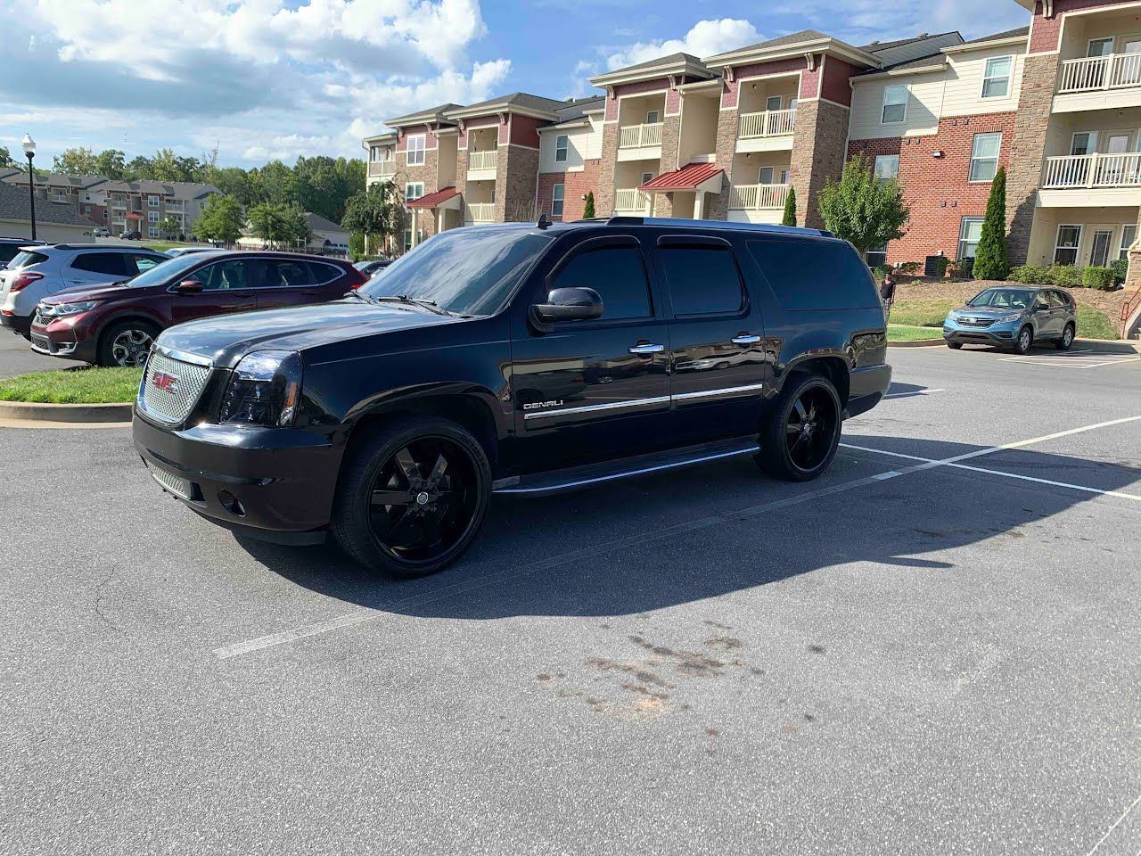 Black GMC Yukon SUV parked in a lot, with apartment building in the background. Sunny day.