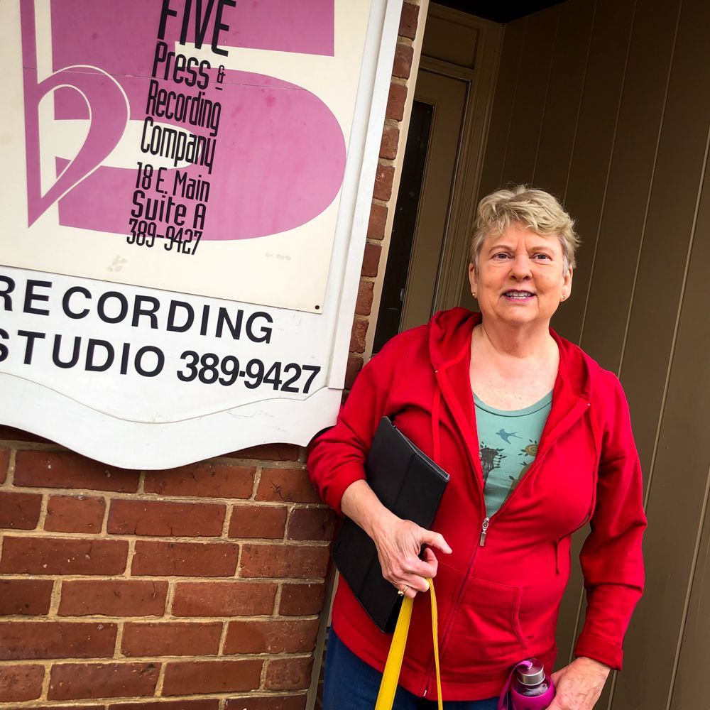 A woman in a red jacket is standing in front of a recording studio