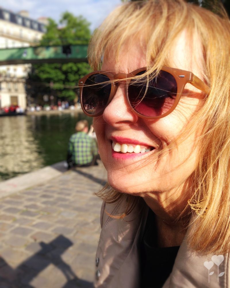 A woman wearing sunglasses is smiling in front of a body of water