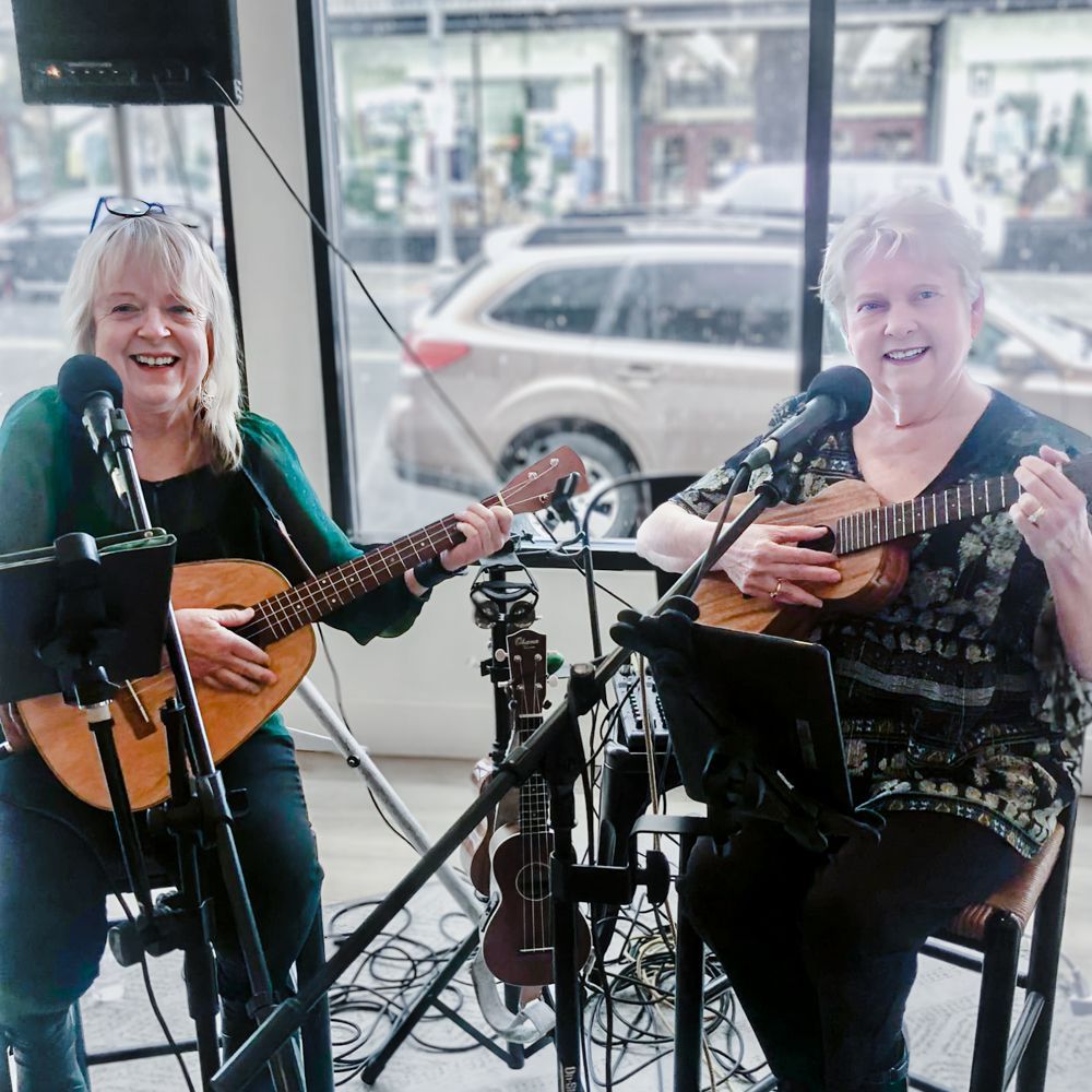 Two women are playing guitars and singing into microphones.