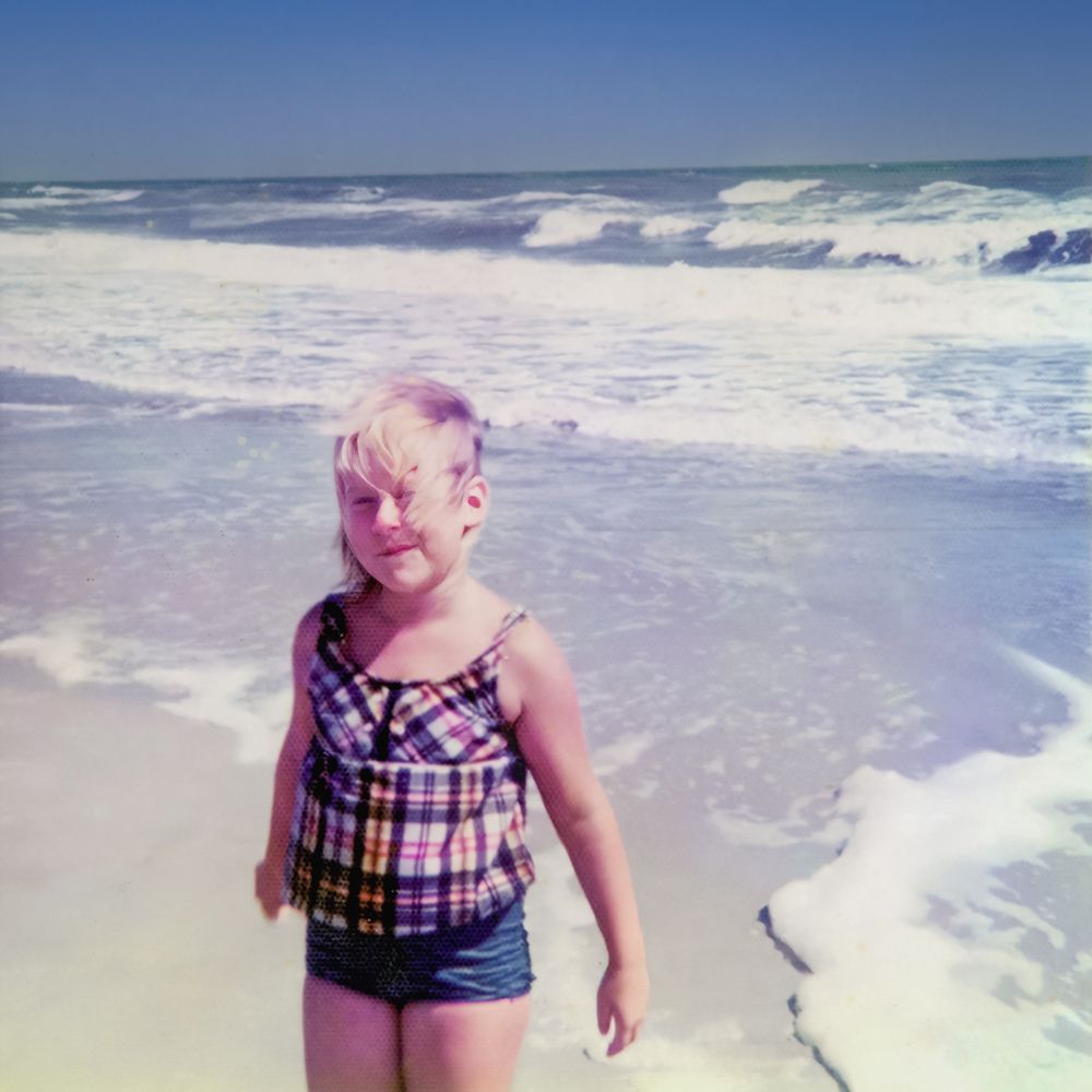 a little girl in a plaid top swimsuit on the beach
