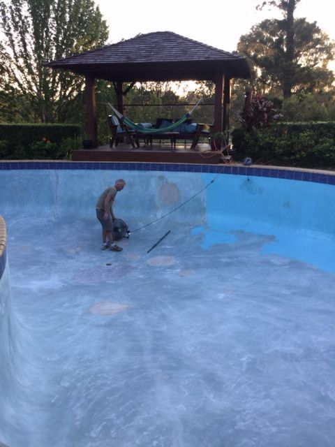 A man is working on a swimming pool with a gazebo in the background