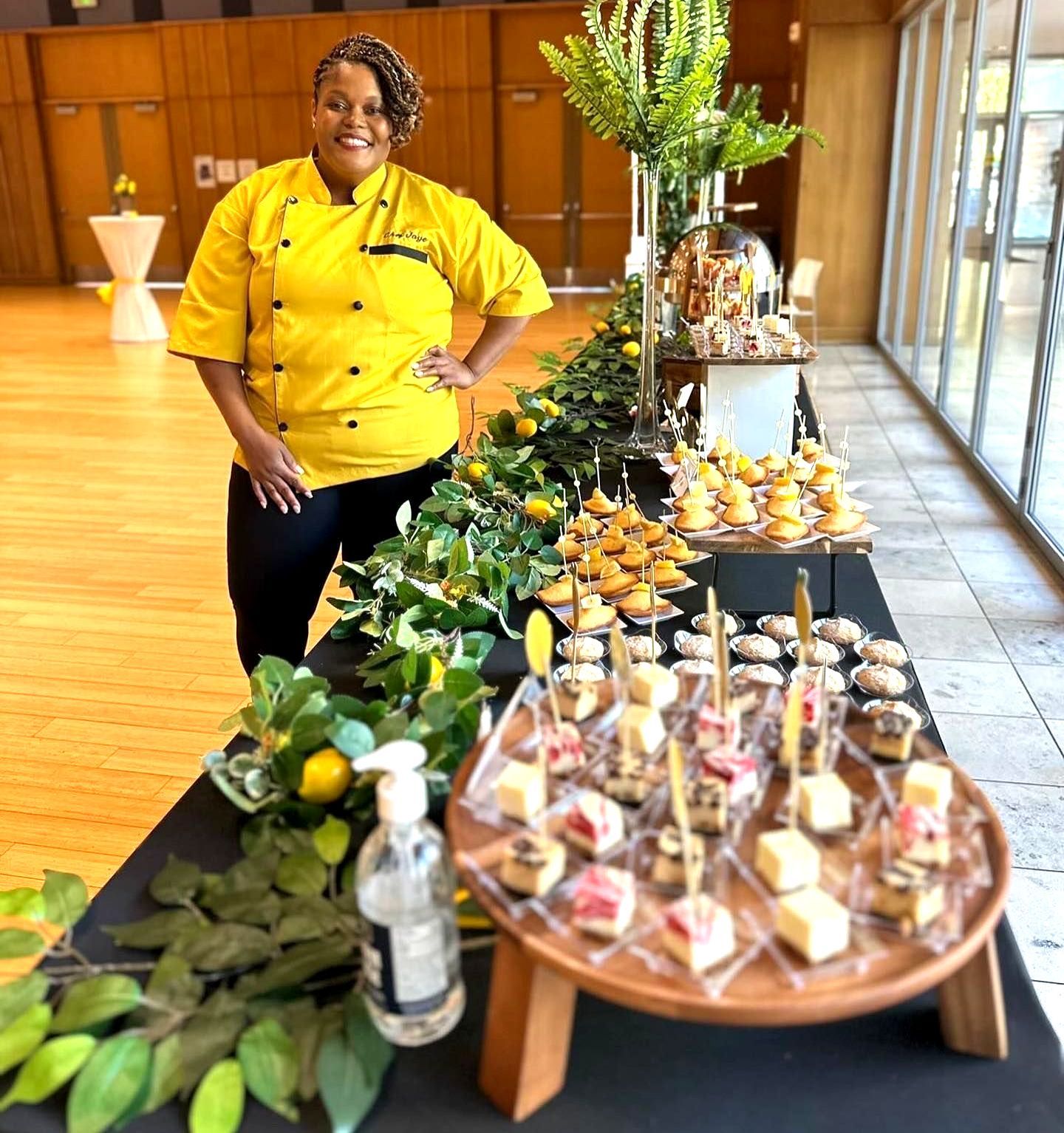 A woman in a yellow chef 's jacket is standing in front of a buffet table.