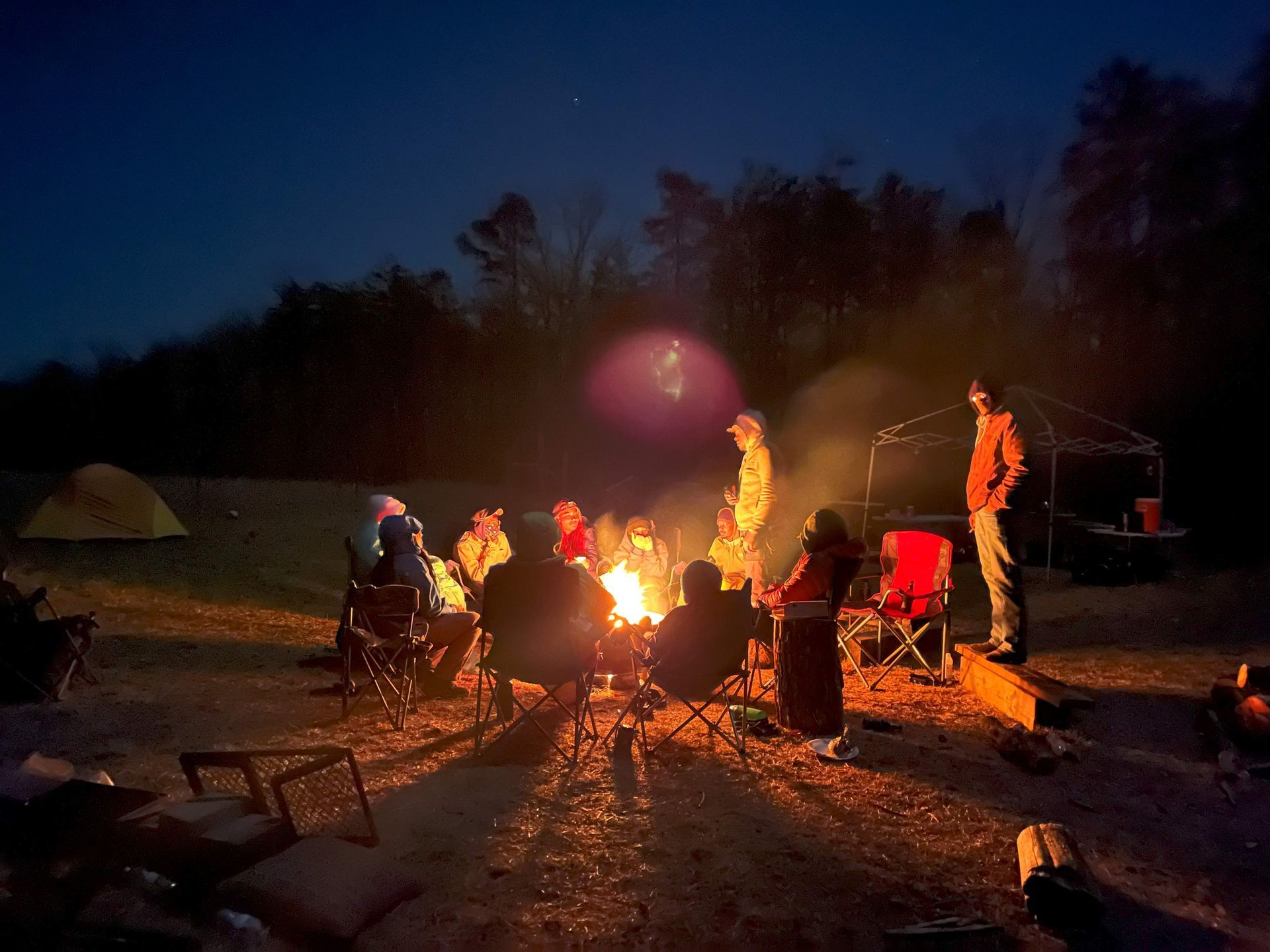A group of people are sitting around a campfire at night.