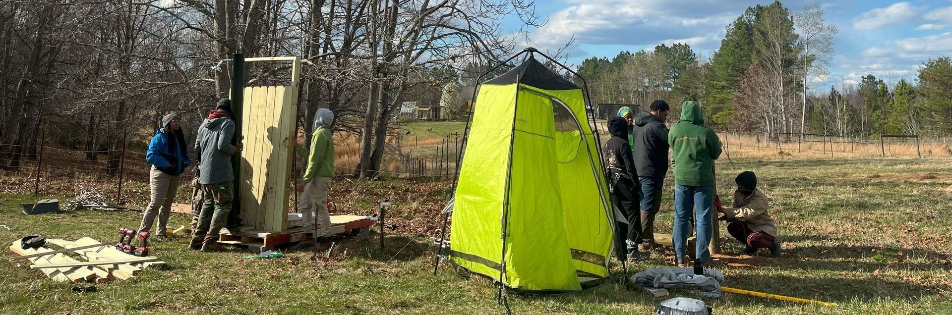 A group of people are standing around a yellow tent in a field.